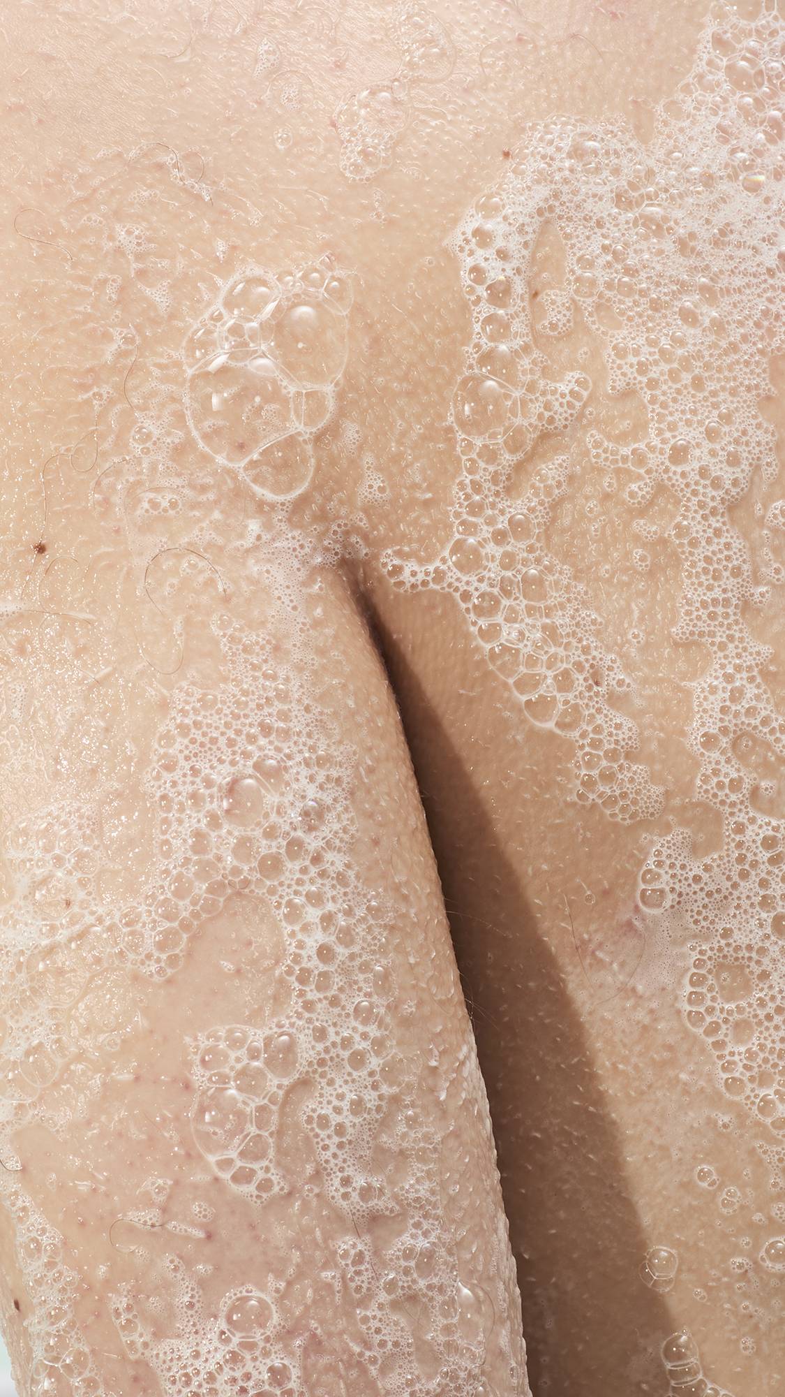 A super close-up shot of a person's arm and shoulder covered in white soap bubbles in the shower. 