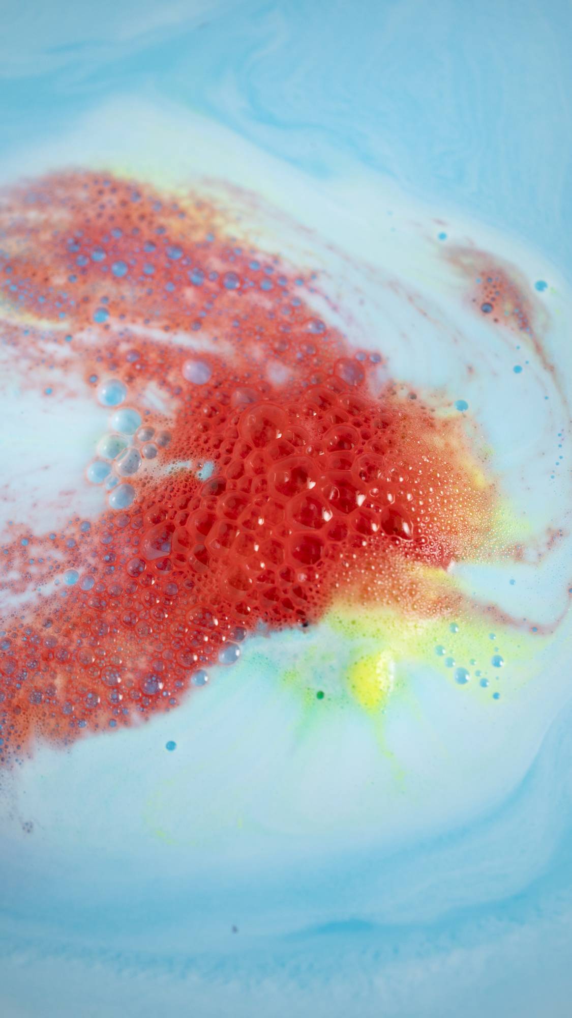 The Super Dad bath bomb is giving off bright fiery, red foamy swirls among the sea of blue.