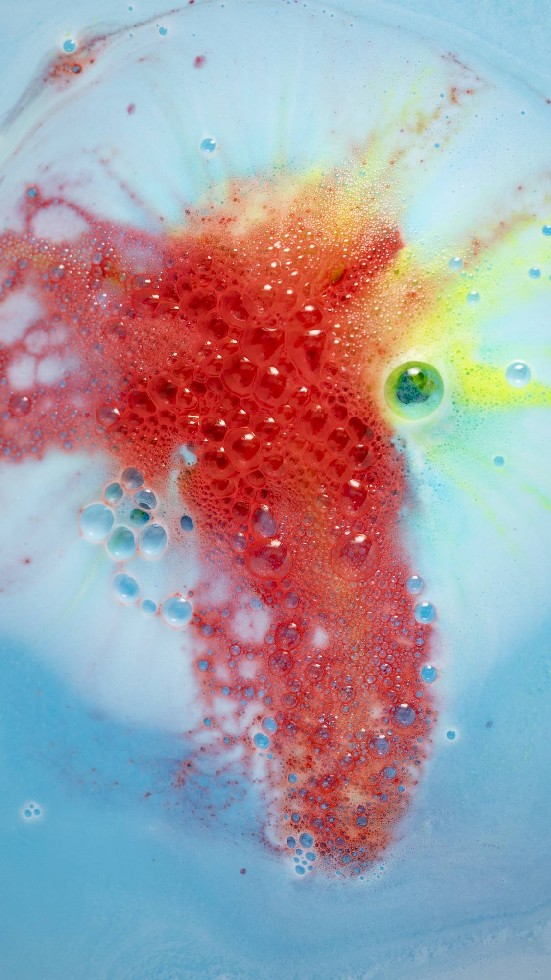 The Super Dad bath bomb is giving off bright fiery, red foamy swirls among the sea of blue.