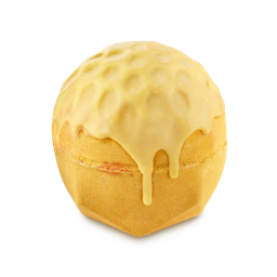 Sweet As Honey. A spherical, golden-yellow bath bomb with a faceted, flat base. It has a honeycomb-textured top that appears to be melting or dripping down the sides like thick honey.