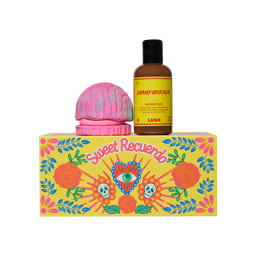 The image shows the 'Sweet Recuerdo' gift set. A colourful folk-art, Día De Muertos-themed box with a heart and skulls sits below a bottle of Champurrado shower gel and a pink and blue Concha Cubbleroon bubble bar, resting on its base.