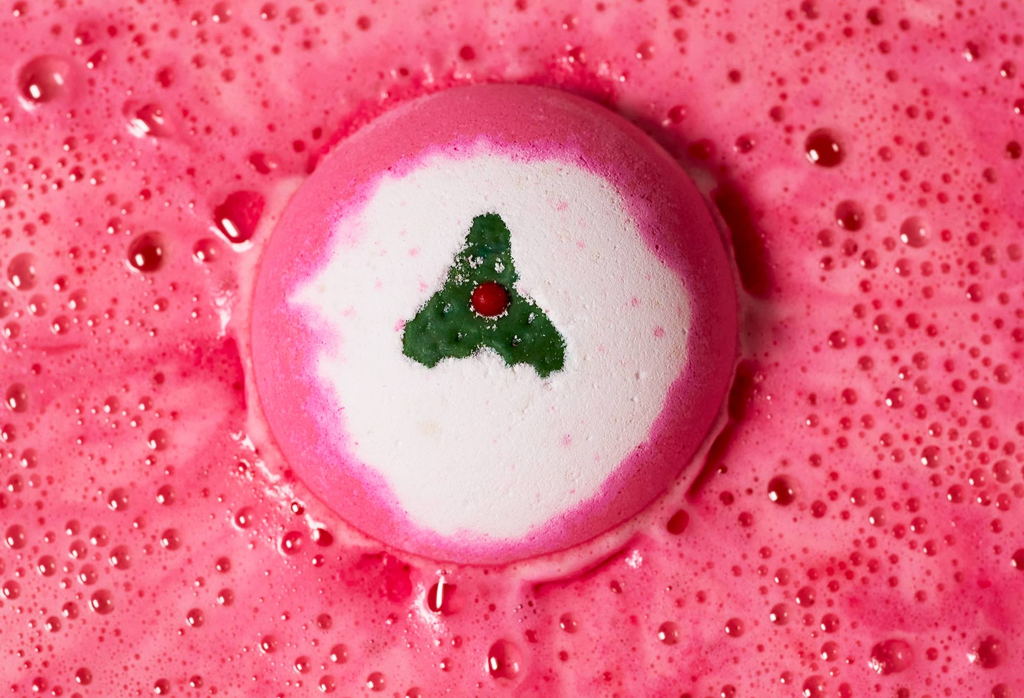 A view from above shows the Sweet Pudding bath bomb in the bath. It sits on a thick blanket of hot-pink foam.