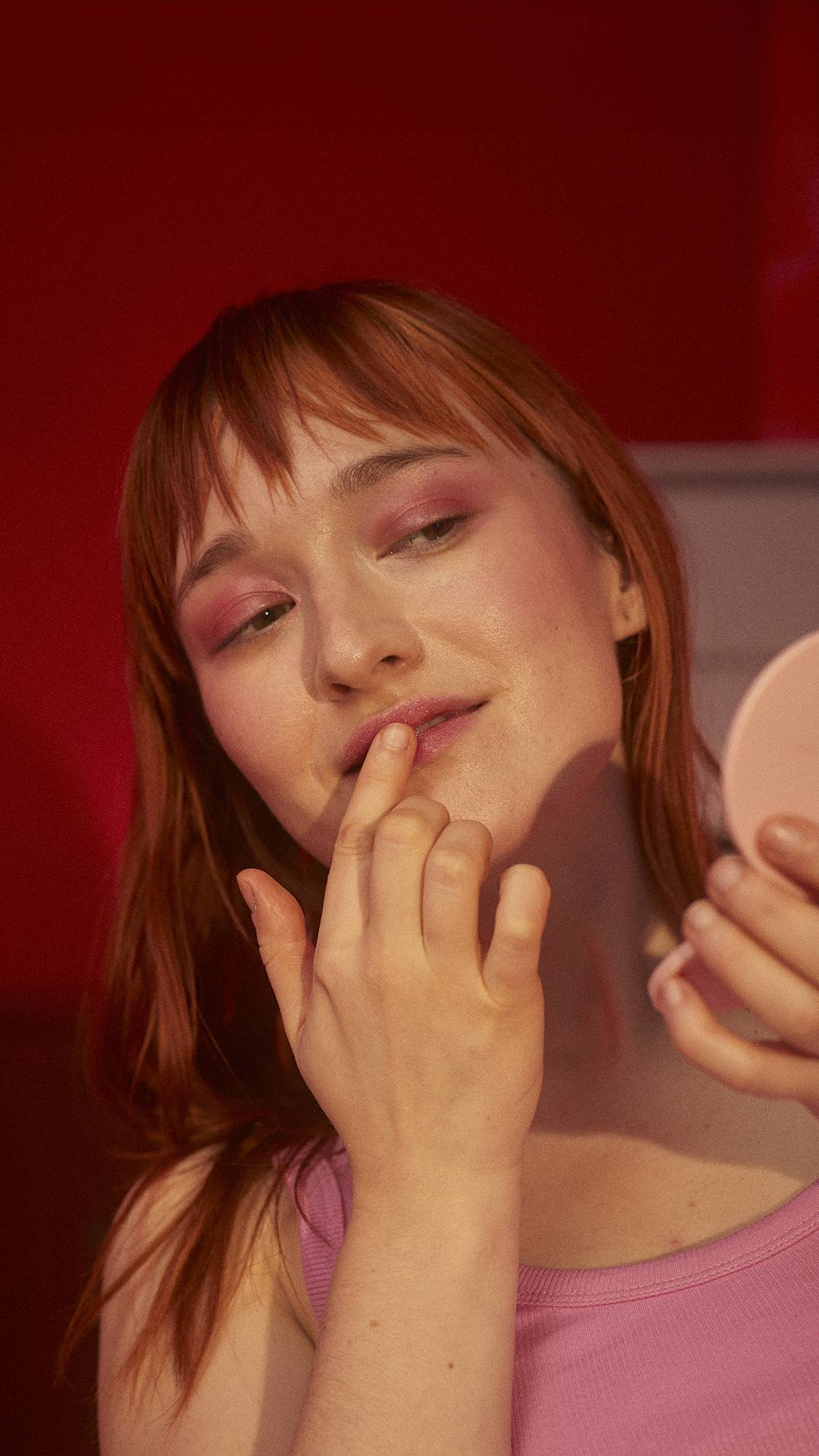 The image shows the model using a compact mirror to apply the Sweet Talk lip scrub. 