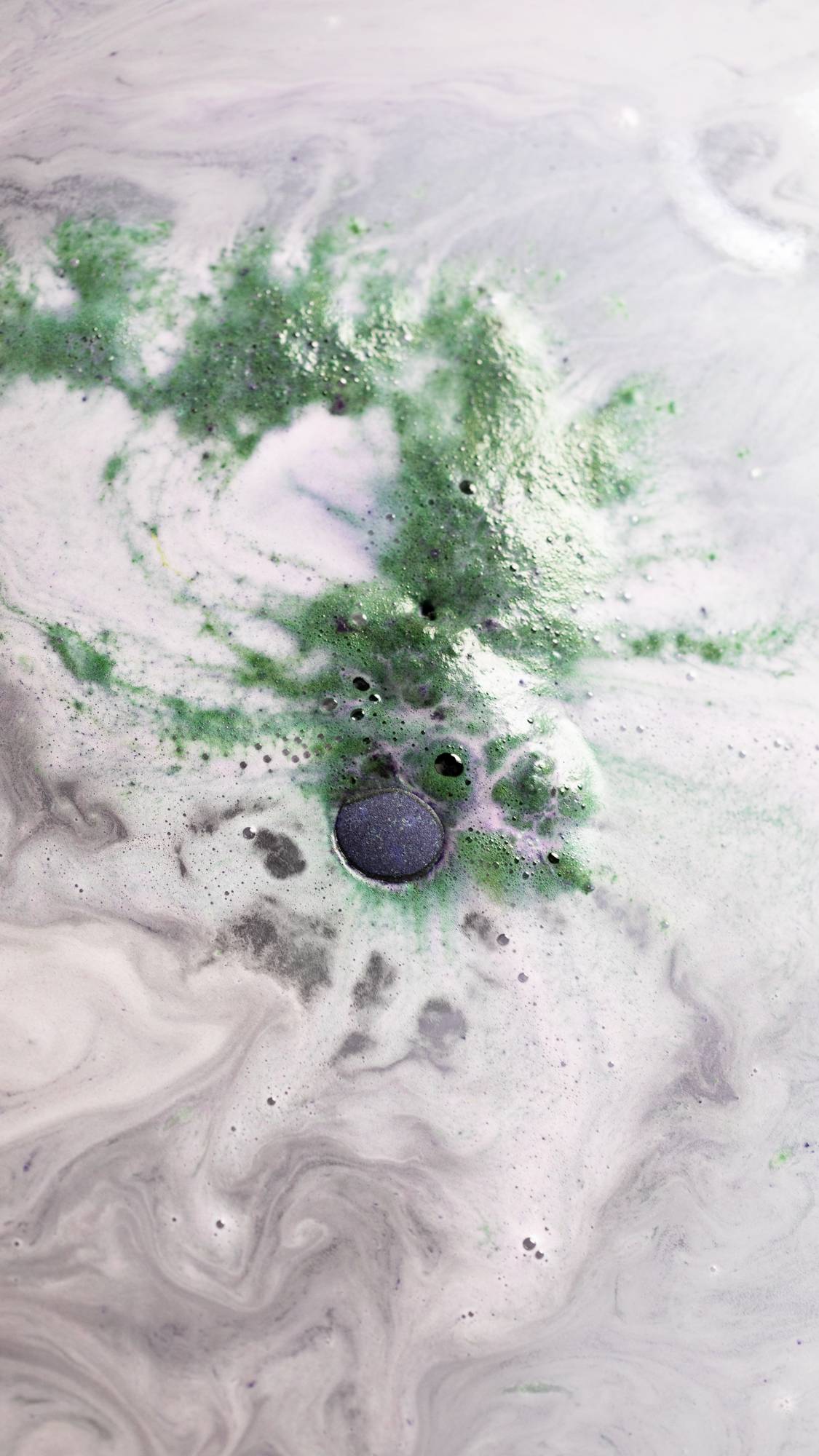 The image shows The Cloud bath bomb almost fully submerged surrounded by velvet foam with bursts of deep green.