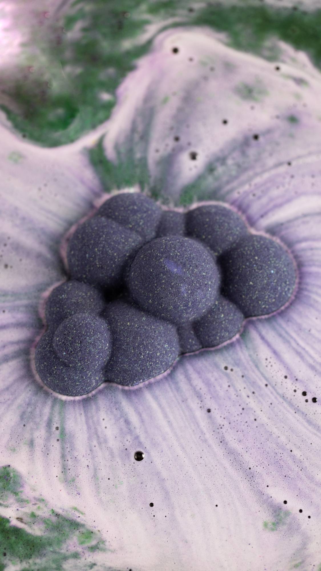 The Cloud bath bombs sits atop the bathwater dispersing enchanting deep purples and green swirls across the surface.