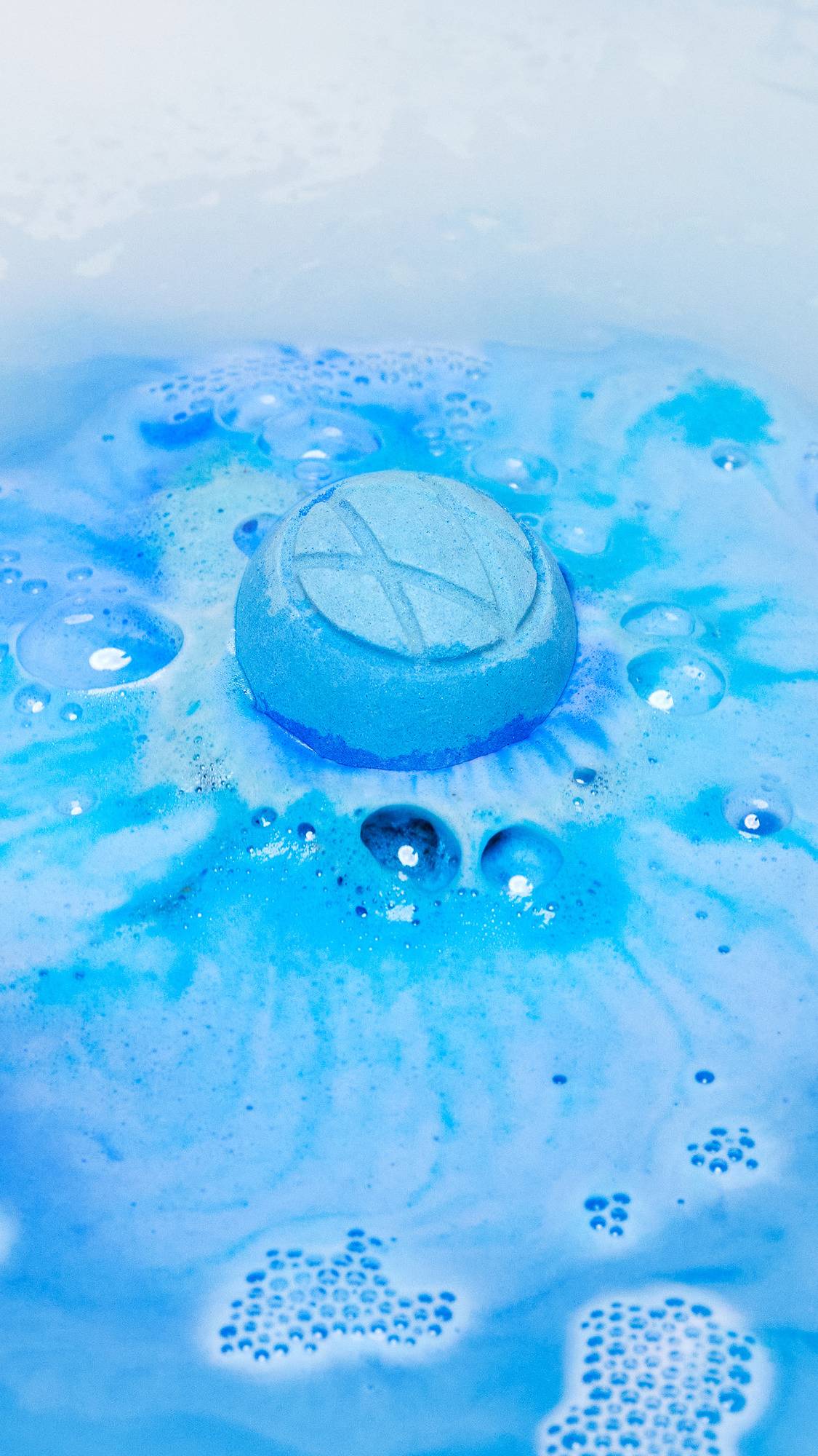 The Hexagon bath bomb has just been placed into the bath water and is giving off a thick foamy layer of blue swirls. 
