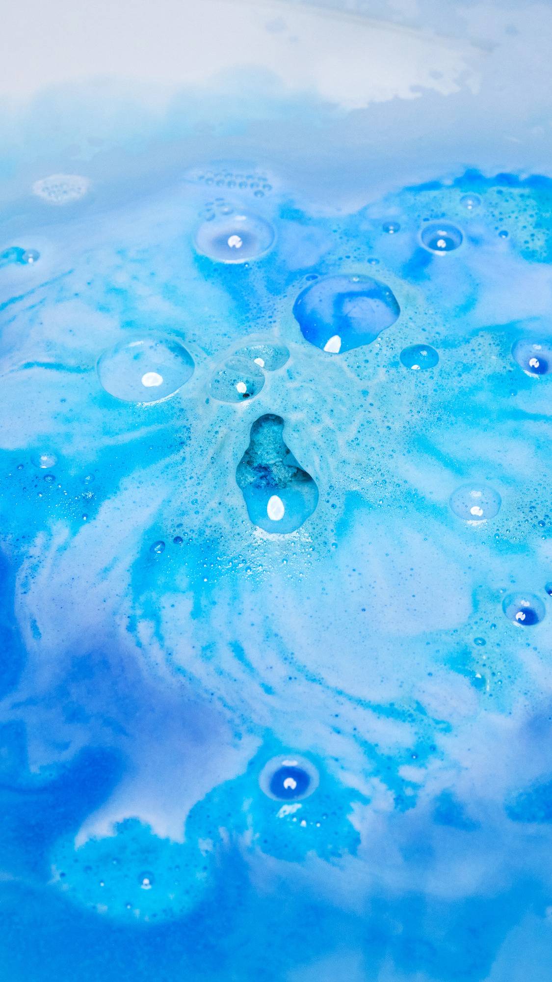 The Hexagon bath bomb is dissolving in the bath water leaving behind ocean-like swirls of deep blues and indigo with lightly foamy bubbles. 