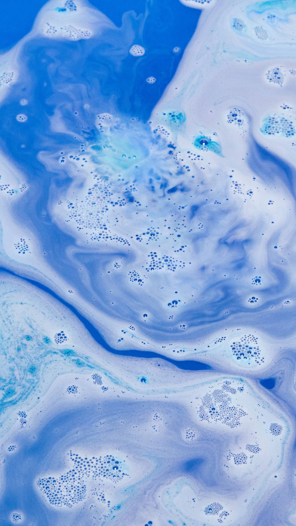 The Hexagon bath bomb is dissolving in the bath water leaving behind ocean-like swirls of deep blues and indigo with lightly foamy bubbles. 