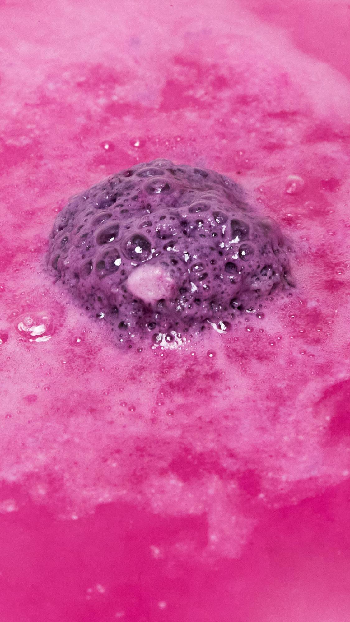The One With Lavender bath bomb is slowly dissolving in the bath water giving off rippling waves of vivid, hot-pink, velvety foam. 