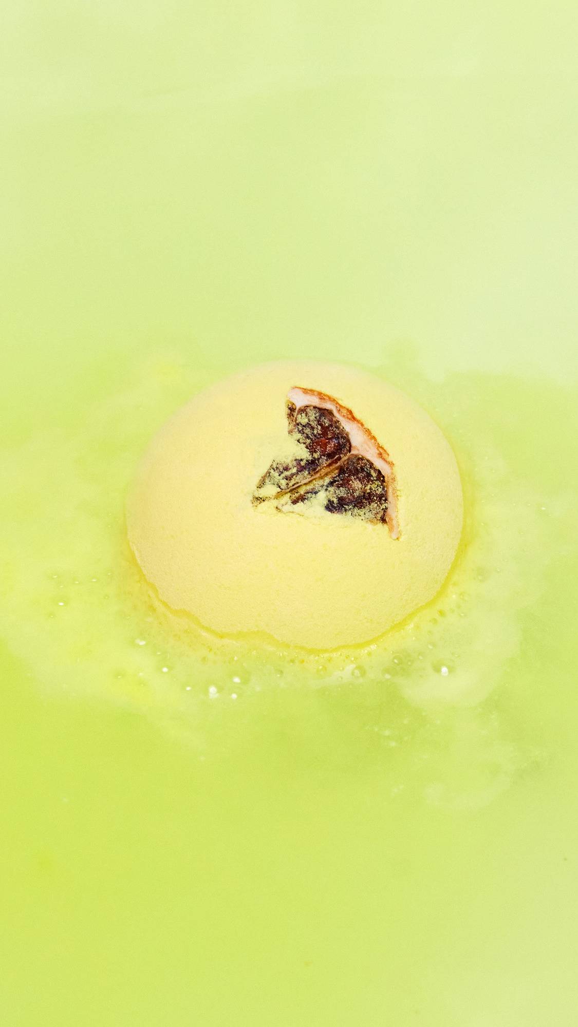 The One With Lemon Oil bath bomb is sitting gently in the bath giving off delicate, velvety, yellow foam across the surface. 