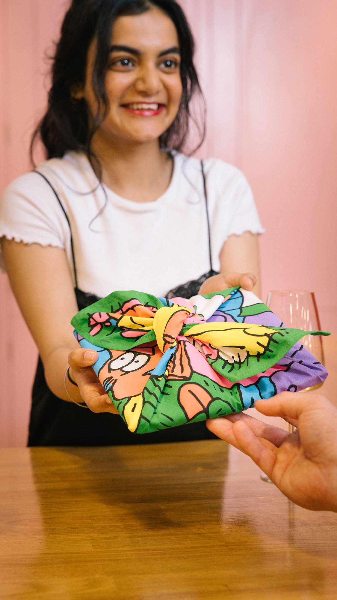Image shows model giving a gift, neatly wrapped in The Picnic knot wrap showing glimpses of fun characters and colours.