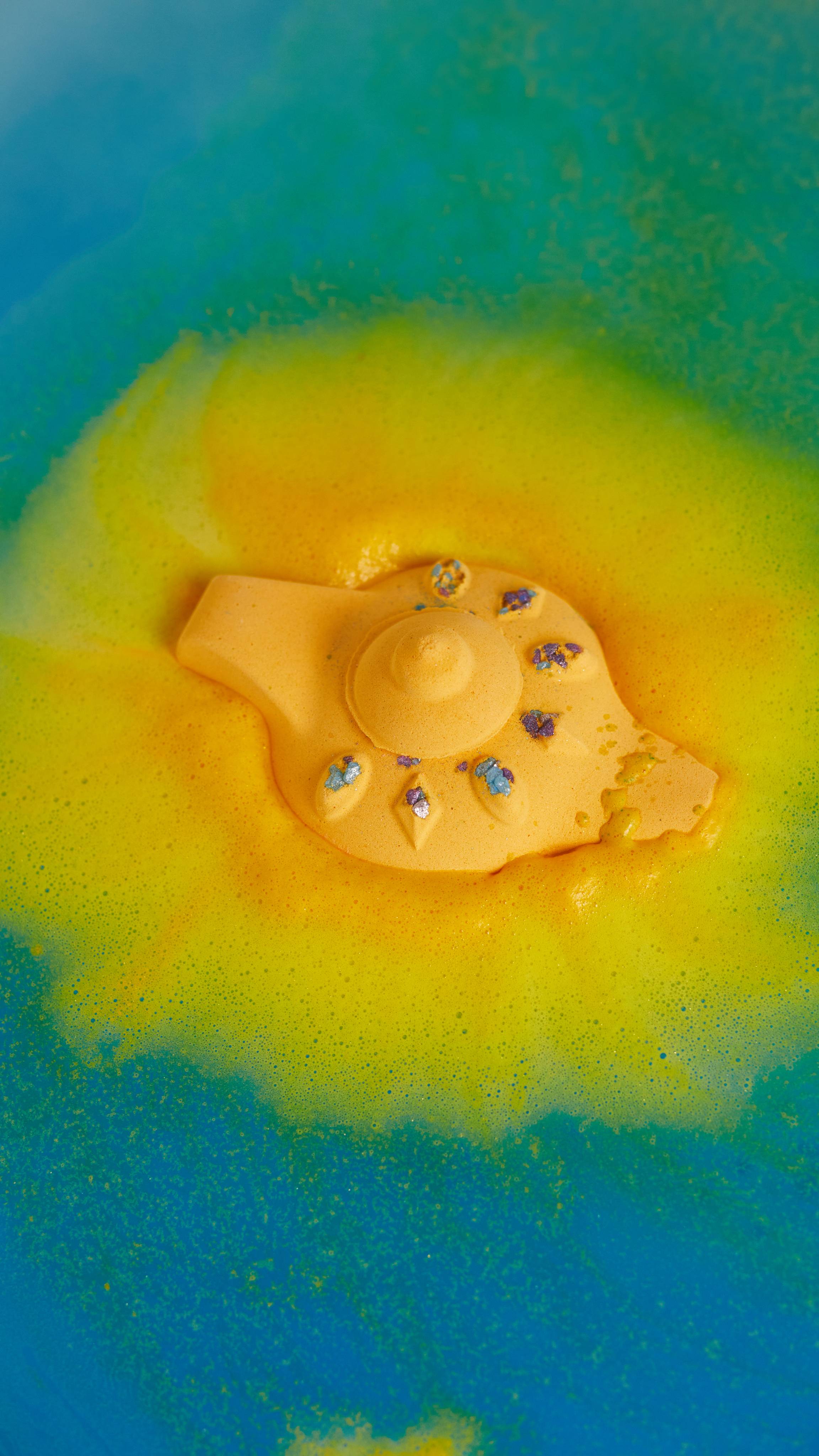 Image shows The Wishing Lamp bath bomb in bath water slowly dispersing its bright yellow outer layer in thick foamy waves.