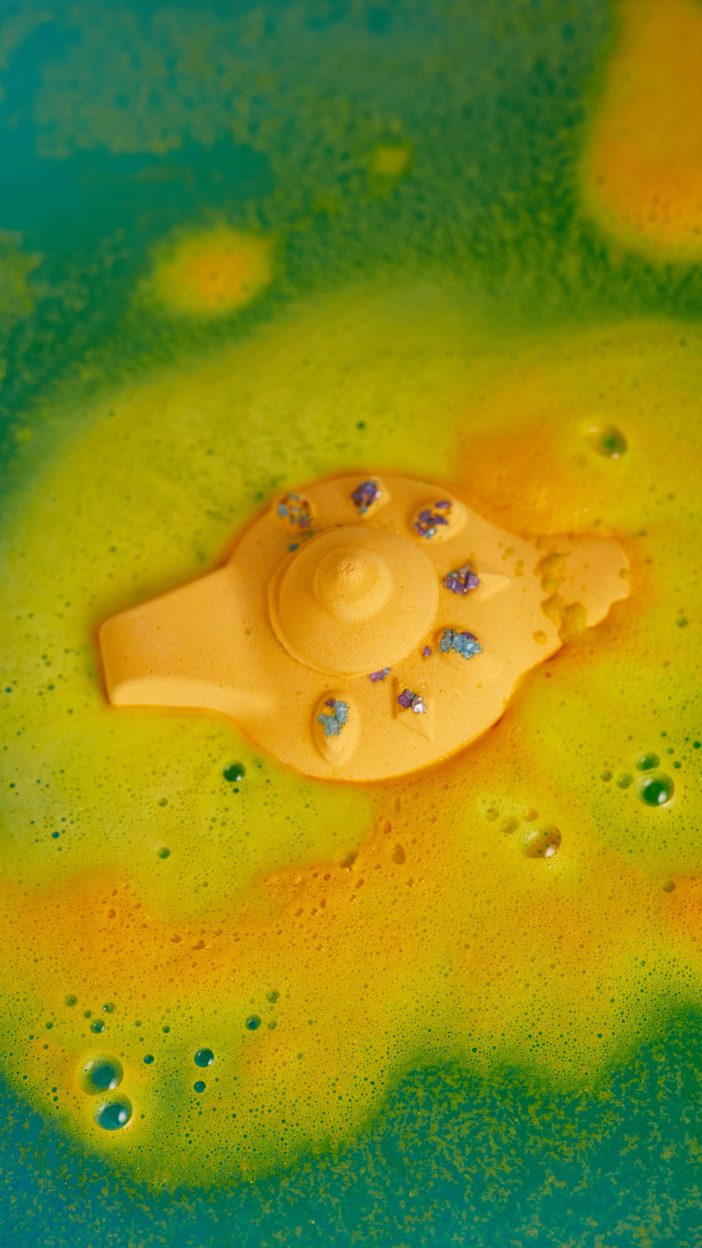 Image shows The Wishing Lamp bath bomb in bath water slowly dispersing its bright yellow outer layer in thick foamy waves.