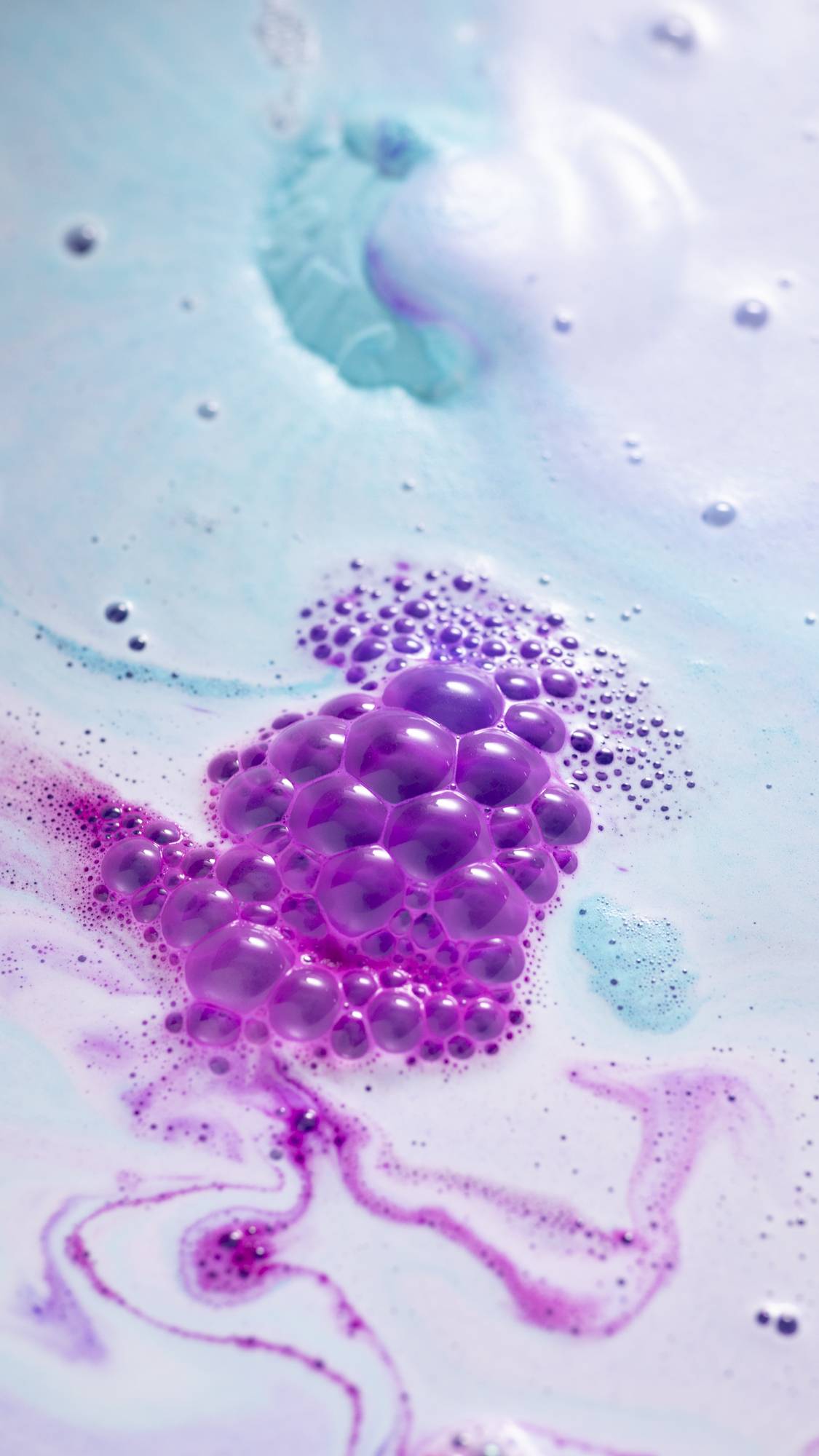 The bath bomb is dissolving in the bath water giving off delicate blue, foamy swirls and a pop of bright pink. 