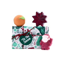 A Lush 'Tis The Season gift set wrapped in green festive paper with red string, featuring an orange Clementine bath bomb, a star-shaped bubble bar, and a red Father Christmas soap