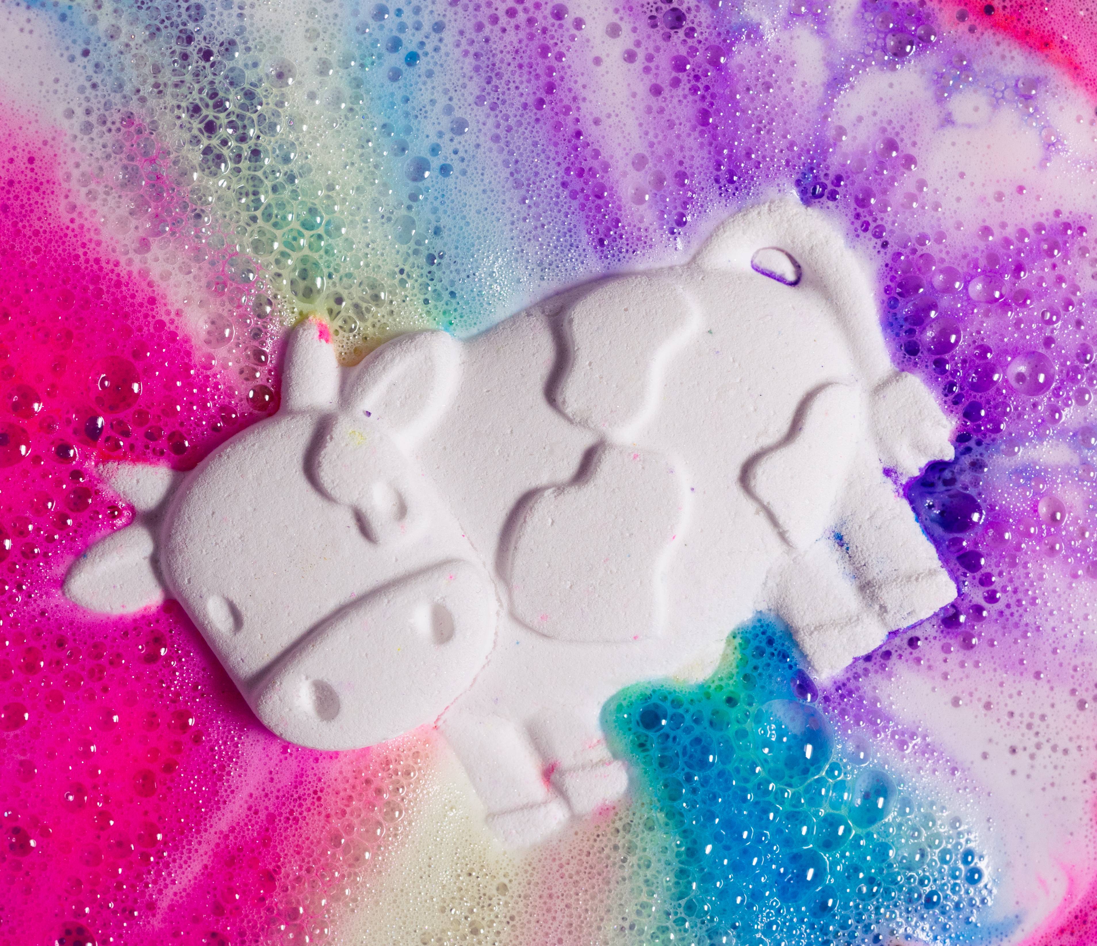 Toby's Magic Cow, a white cow-shaped bath bomb, lies back in a foamy rainbow-coloured water of its own fizzing creation.