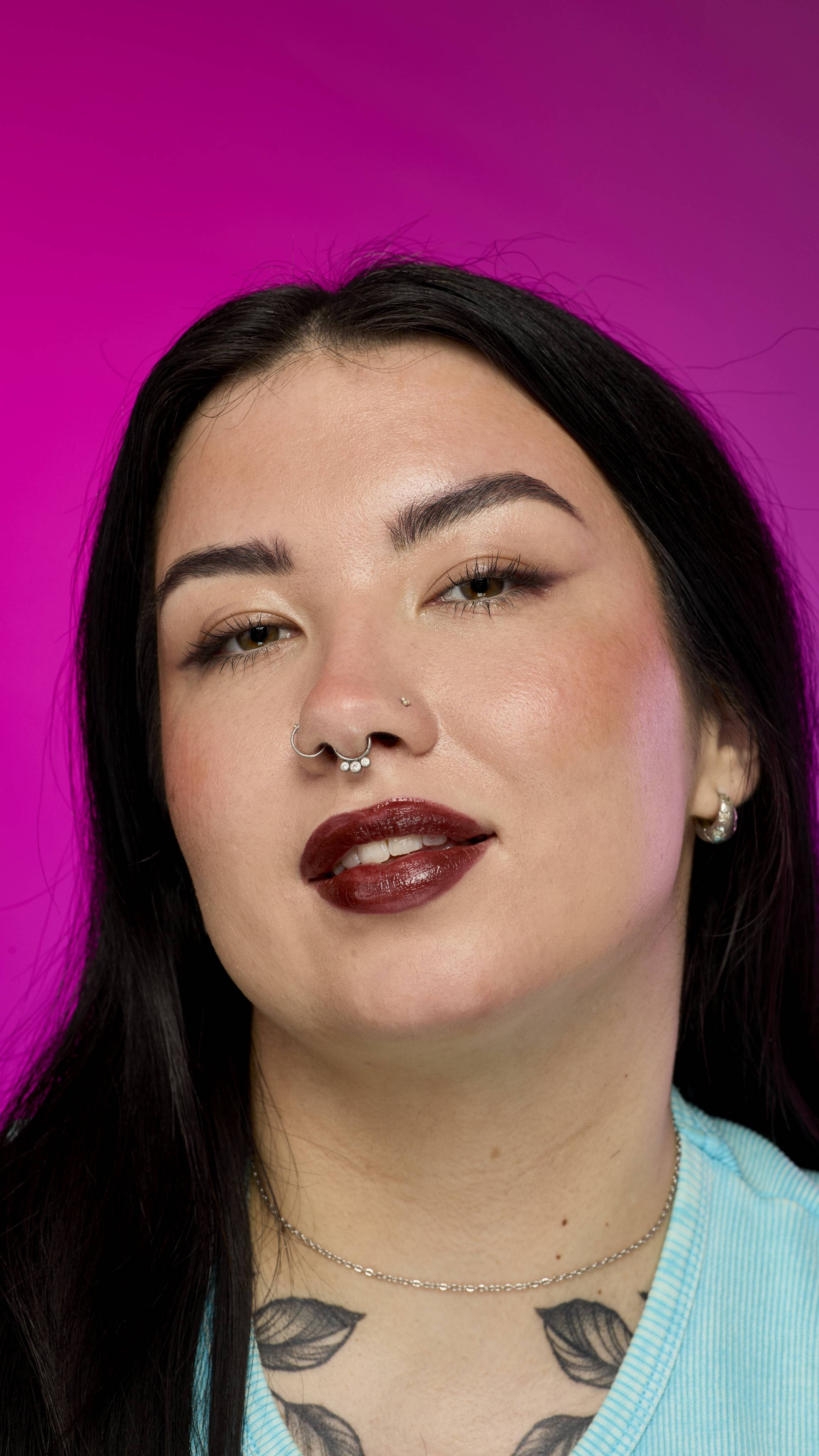 The image shows a model with long, dark hair on a vibrant magenta background, from the neck up. They are wearing the rich, dark chocolate-coloured Toffee Apple lipstick.
