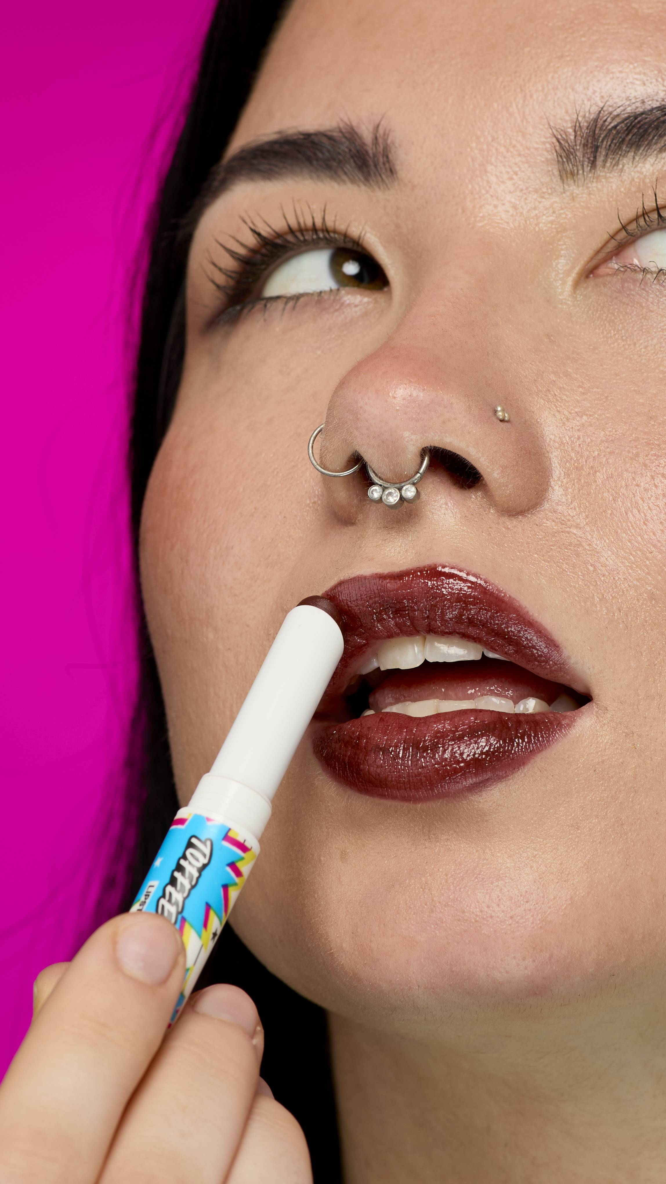 A close-up shot of a model with long, dark hair. They are looking away as they apply the rich, chocolate-coloured Toffee Apple twist-up lipstick.
