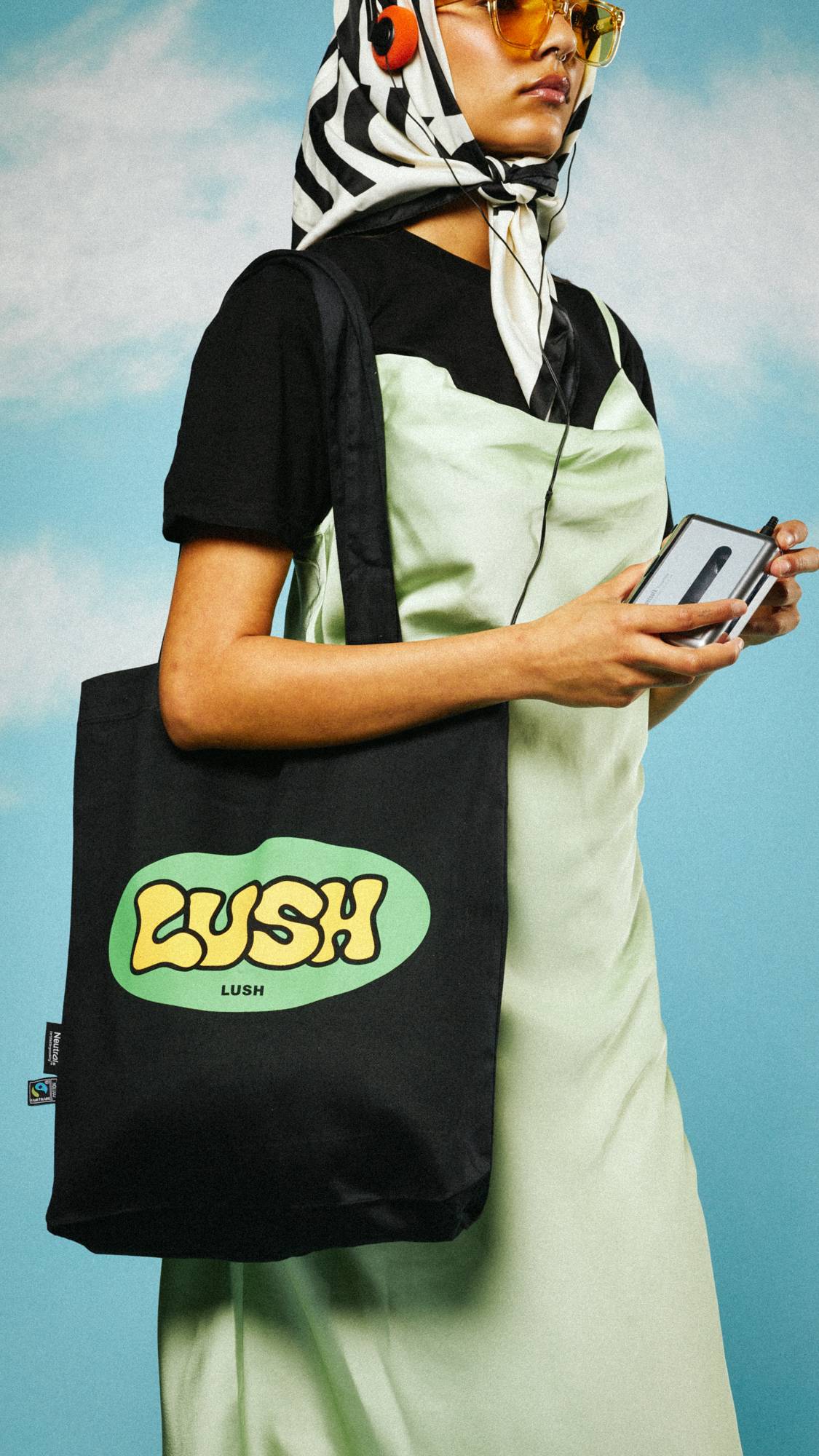 Model is stood on a sky-like background with a head scarf and headphones, wearing the Retro Bubble tote bag.