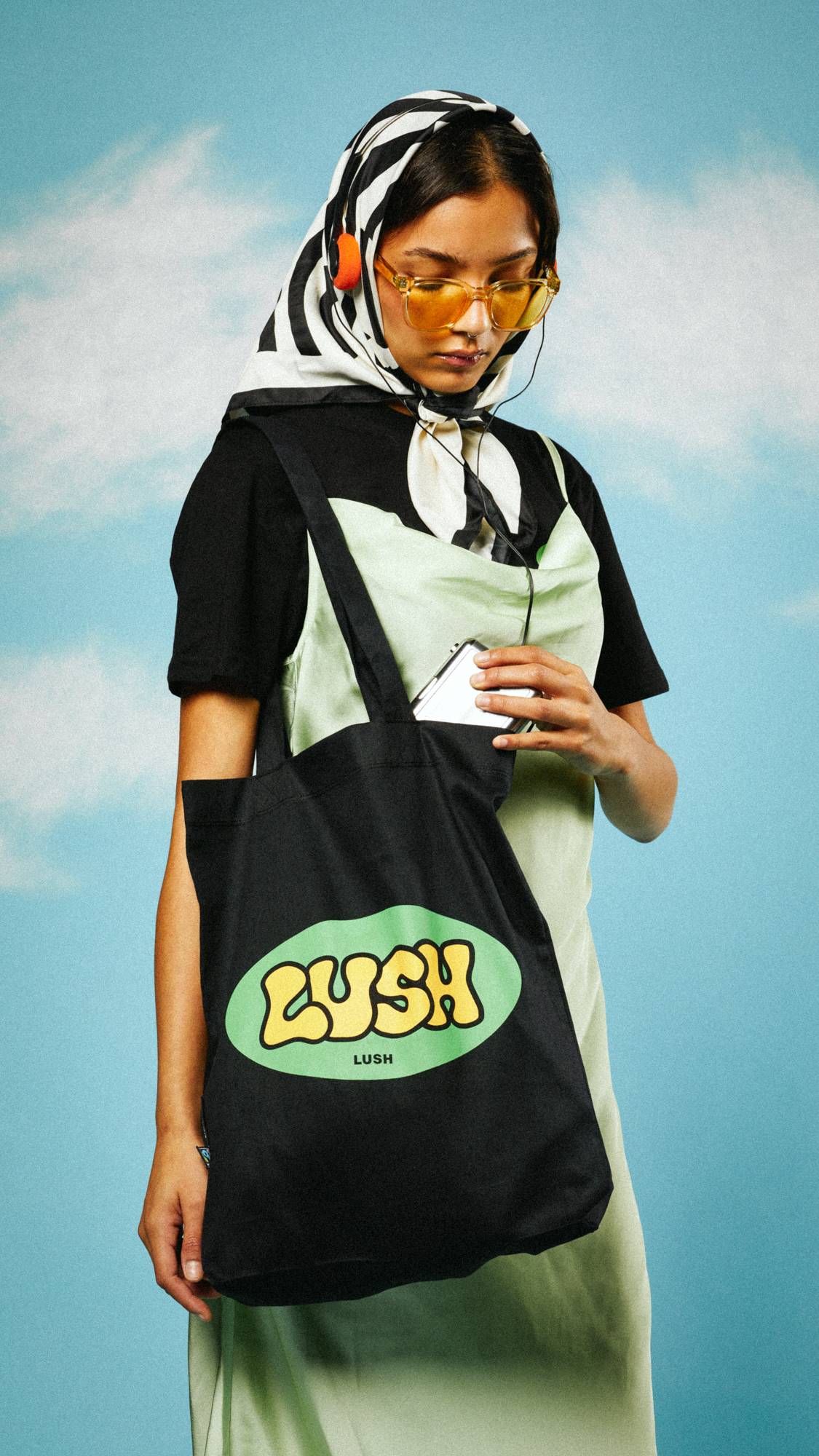 Model is stood on a sky-like background with a head scarf and headphones, wearing the Retro Bubble tote bag.