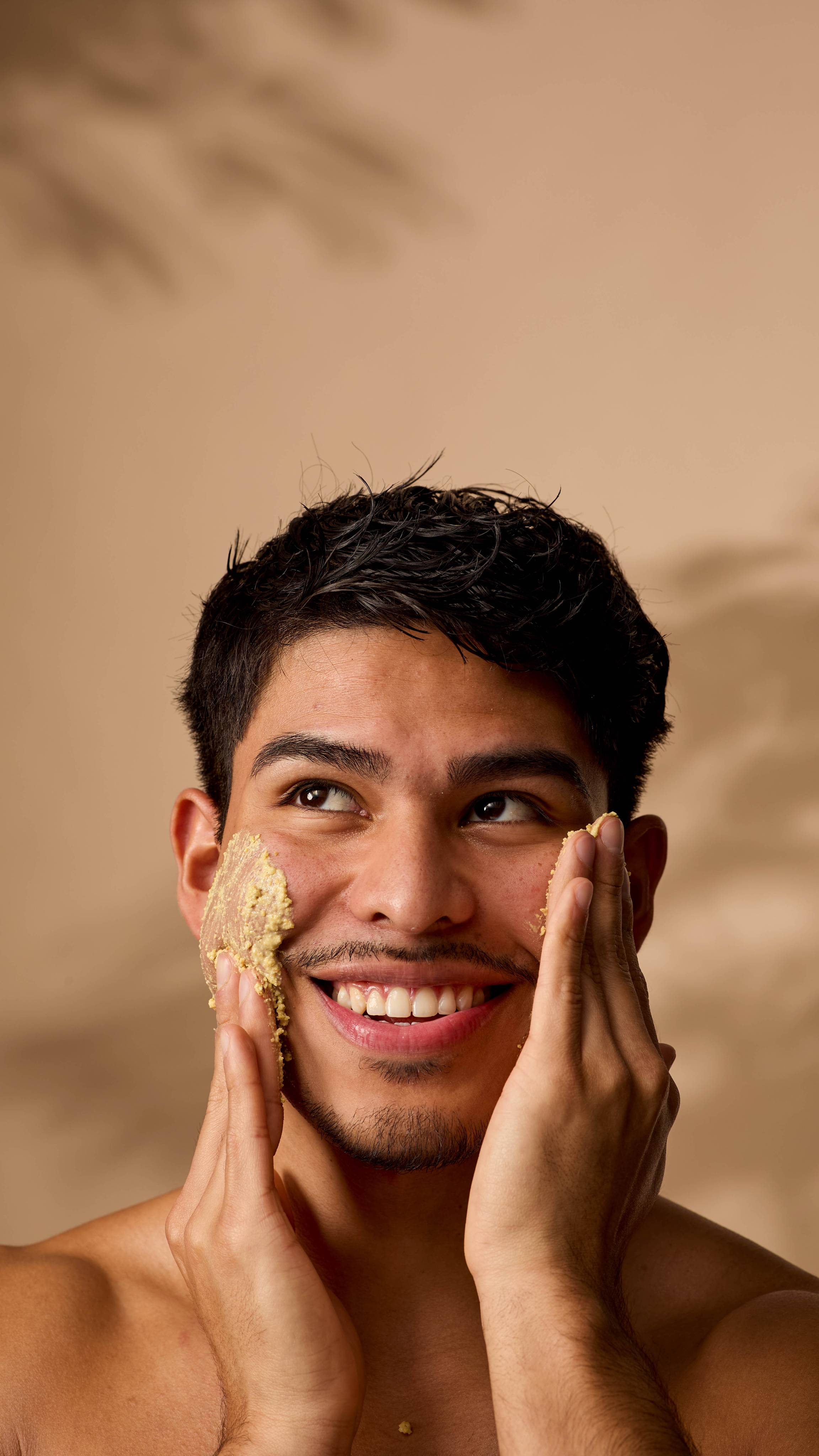 The model is smiling and looking upward as they apply the Turmeric Roll cleanser to both cheeks under warm lighting. 