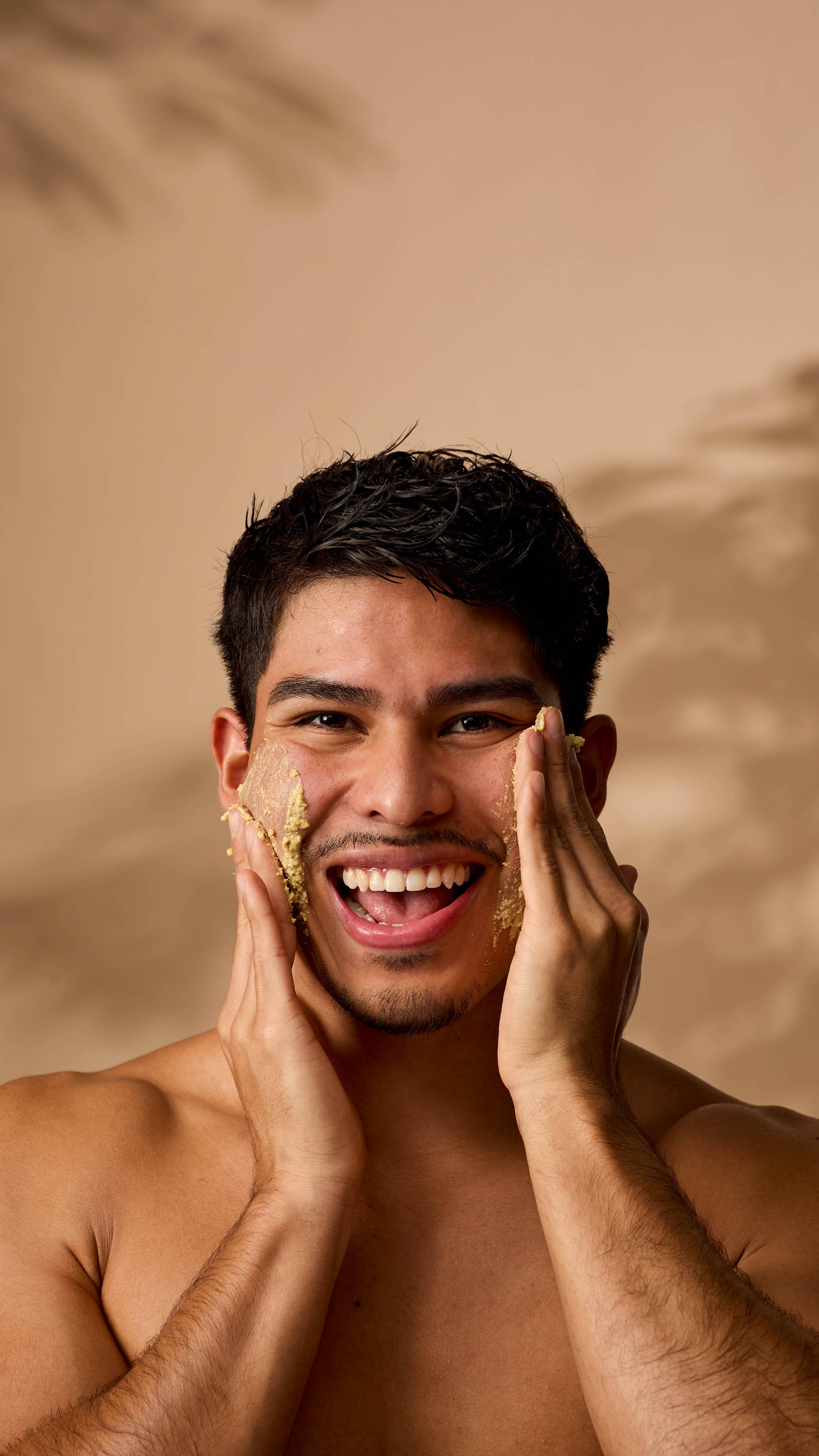 The model is smiling and looking forward as they apply the Turmeric Roll cleanser to both cheeks under warm lighting. 