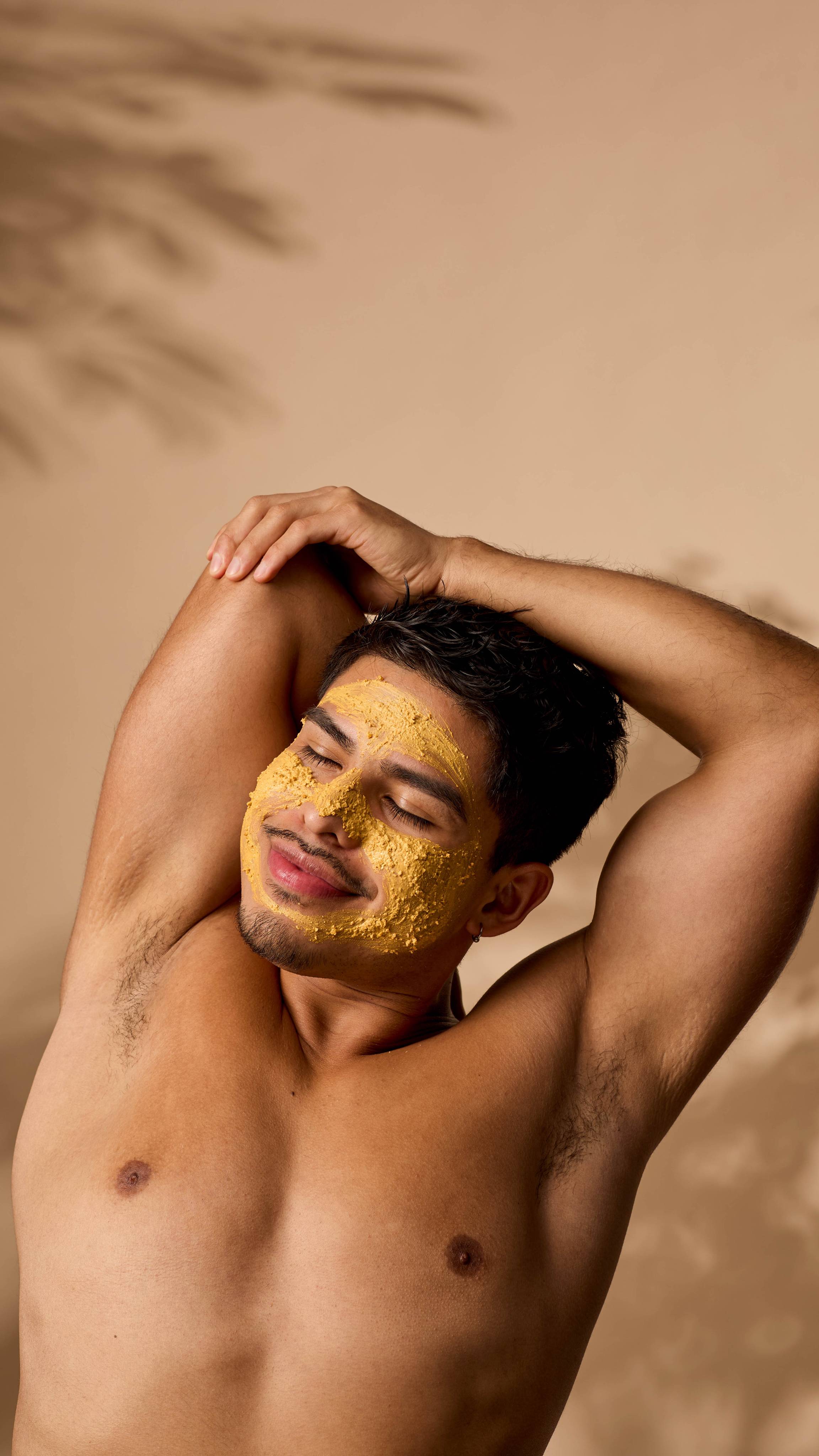The image shows the model stretching with their eyes closed as their face is evenly covered in the Turmeric face mask.