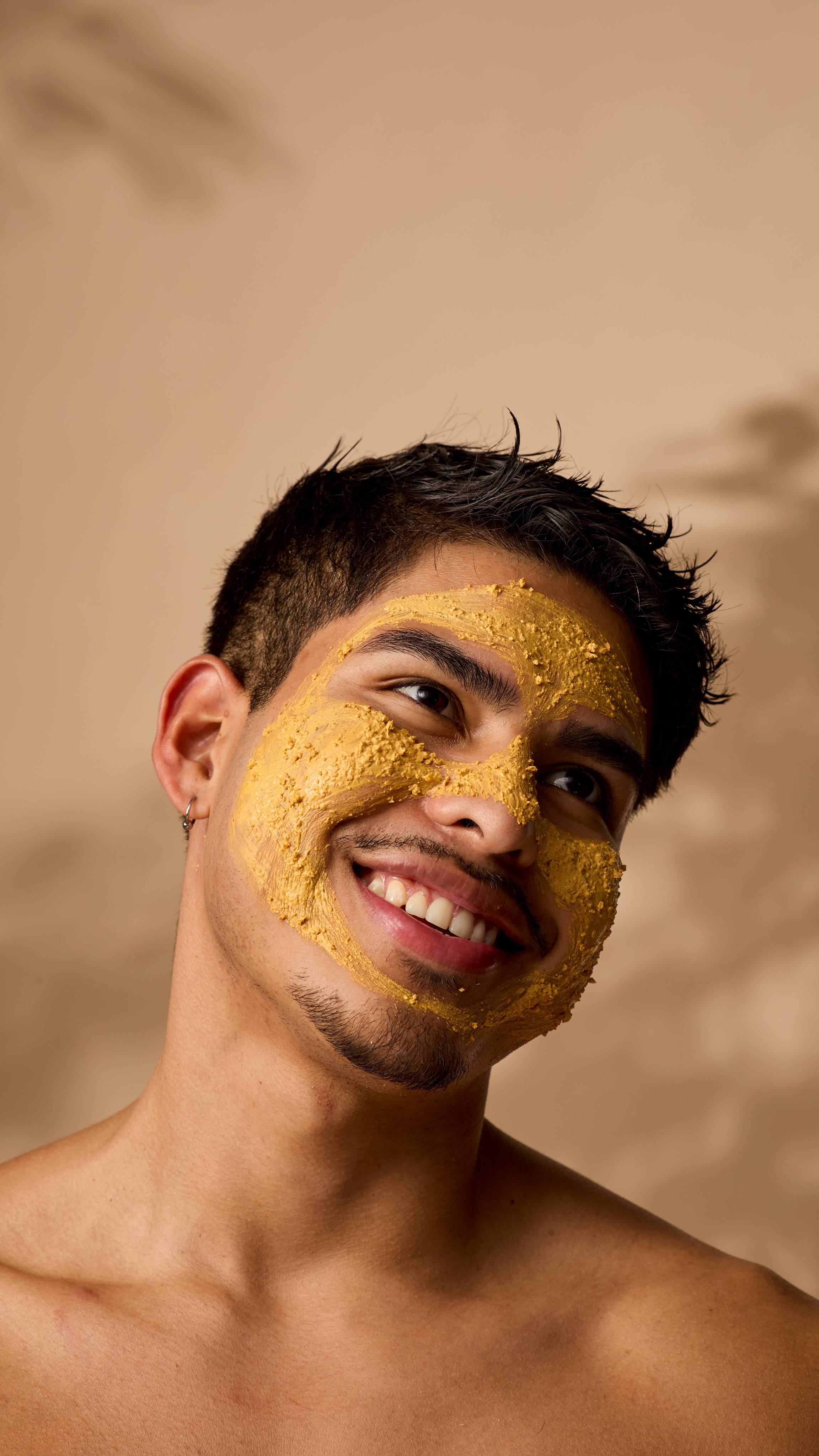 The image shows the model smiling into the distance as their skin is coated with the Turmeric face mask.