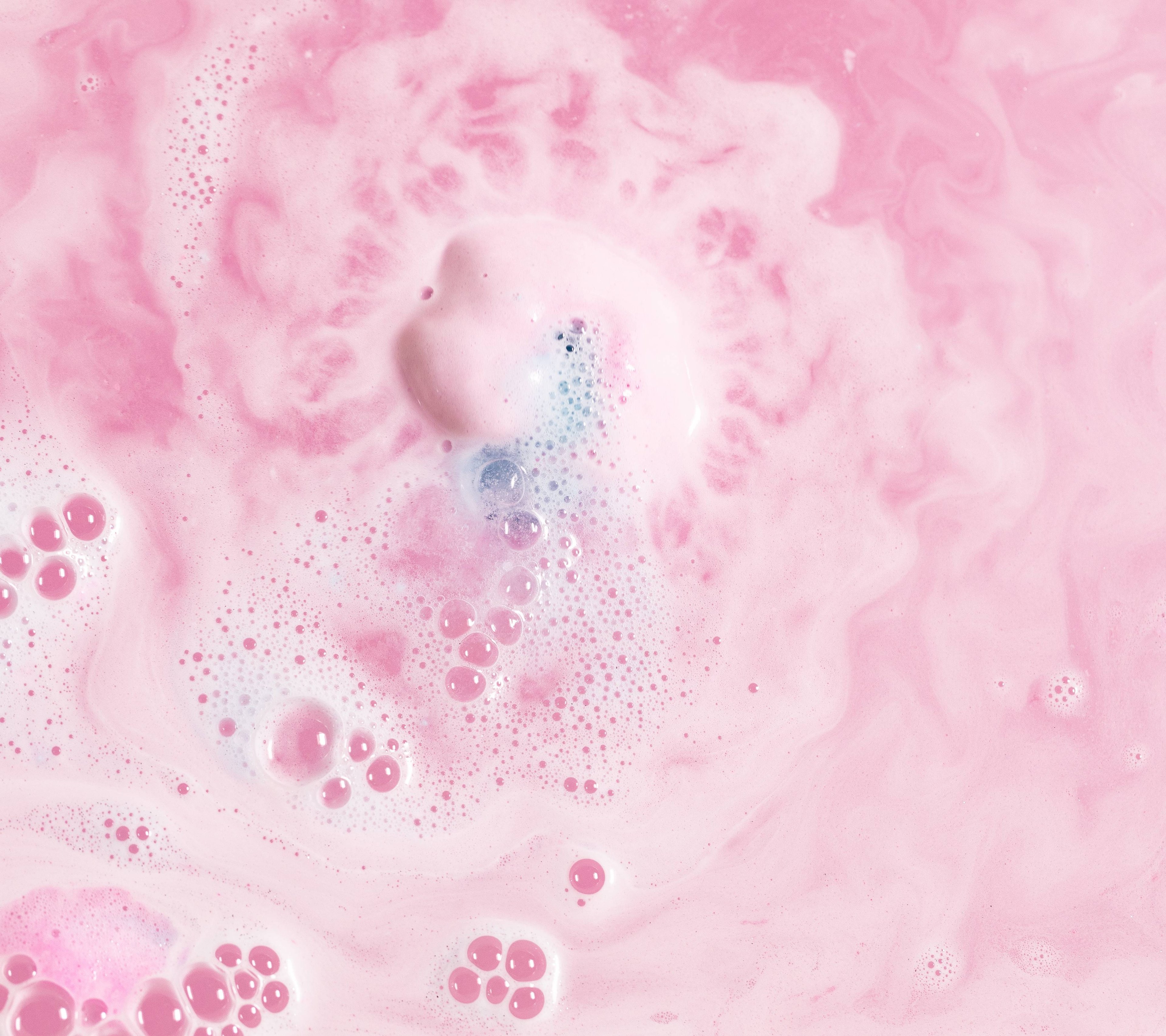 The Twilight bath bomb is slowly dissolving in the bath water creating thick swirls of delicate pink, bubbly foam with a flash of blue. 