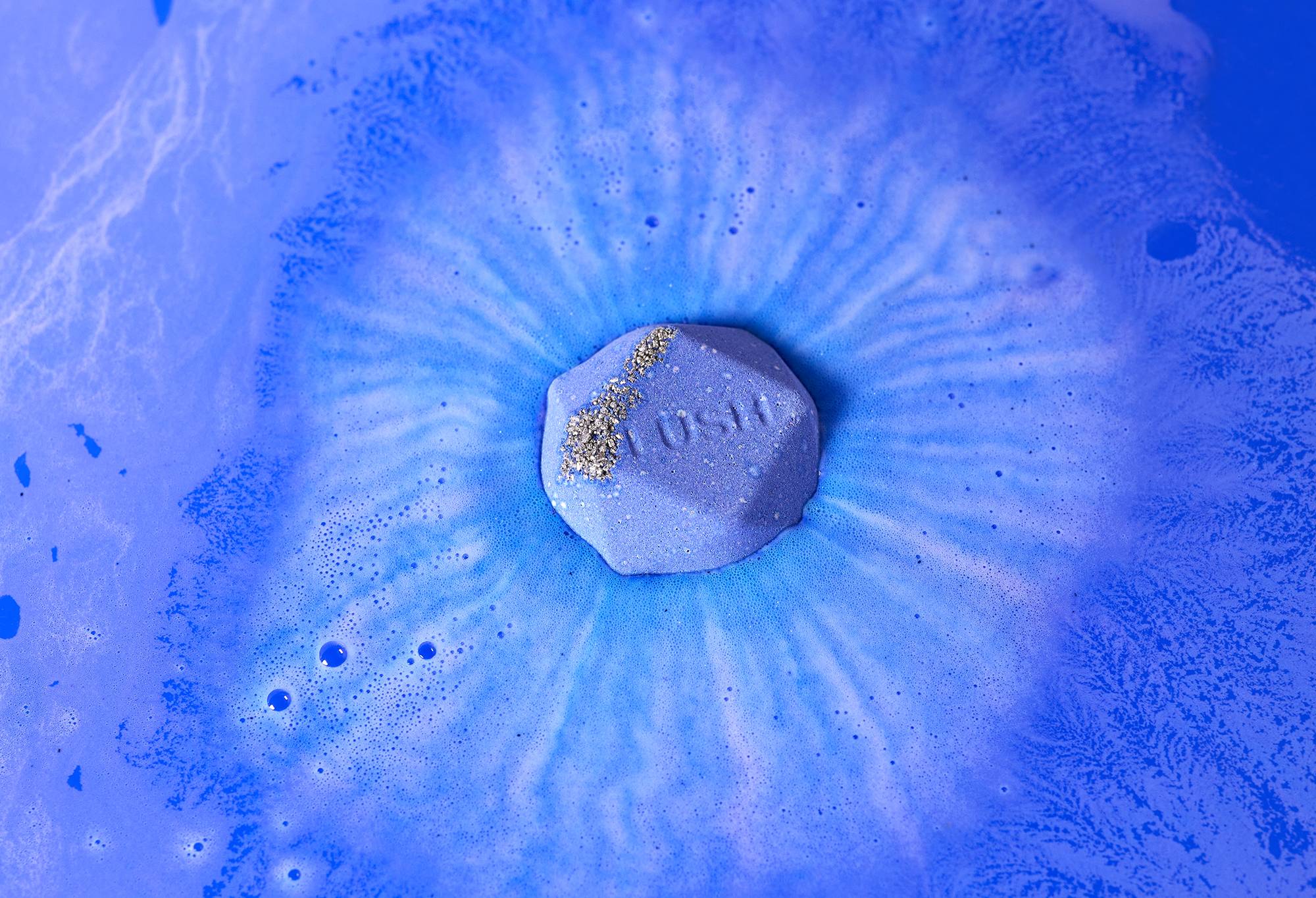 Uchumizu bath bomb floats among deep blue swirls with blue-coloured sugar and "Lush" embossed on top.