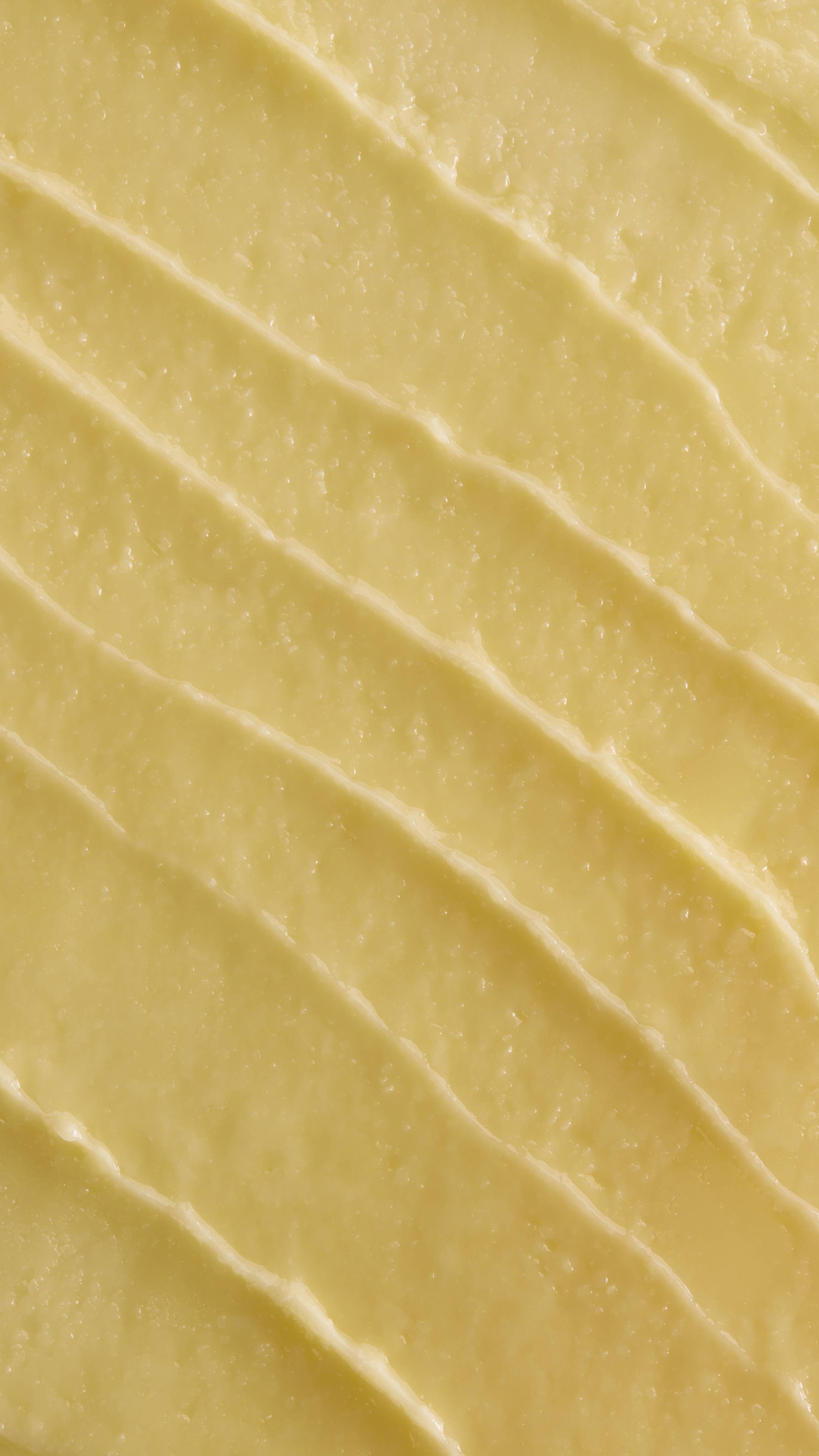 A close-up, aerial shot of thick, pale yellow 'Ultraplant' facial cleanser. The product is spread out in several diagonal, textured ridges, showing its smooth yet slightly granular, buttery consistency. 