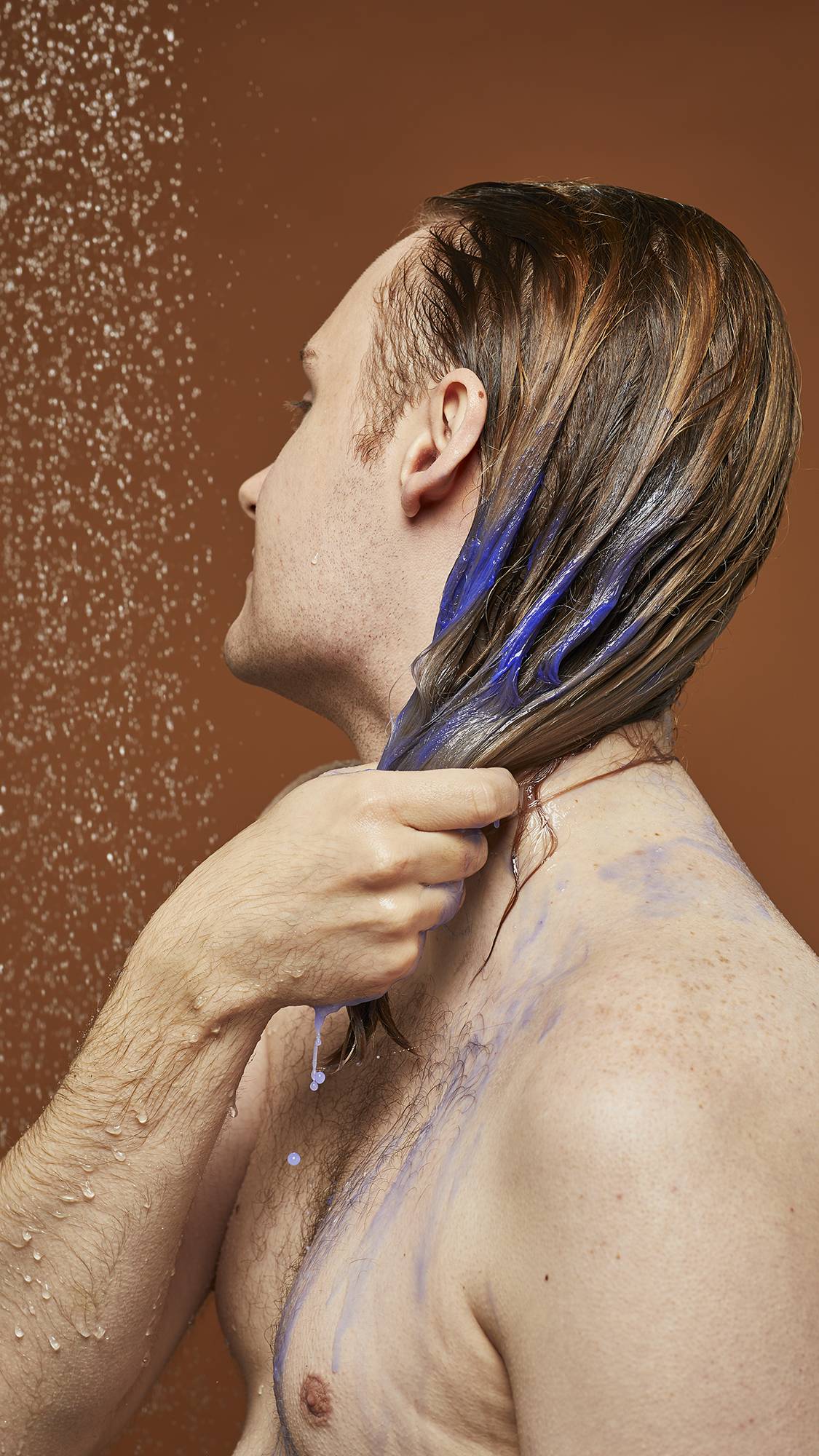 Model is stood in the shower soaking the mid-length and ends of their hair with the vibrant Violet cream shampoo.