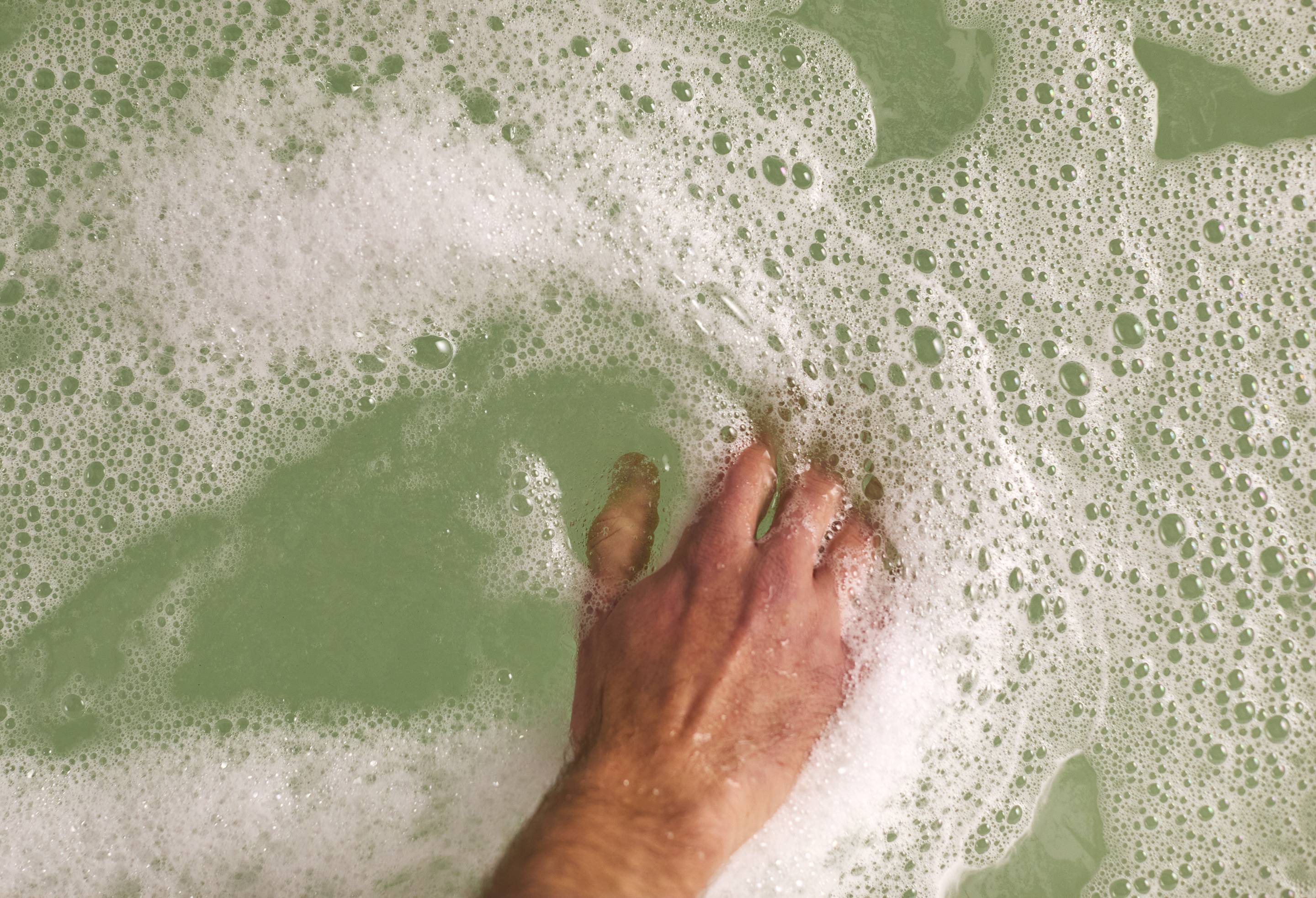 The image shows the model's hand gently stroking the bubbly, green water created by the Wash And Grow bubble bar.  
