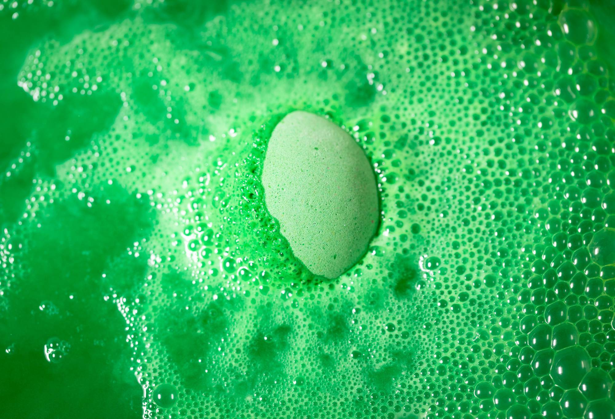 Wild Remedy bath bomb is slowly dissolving as it creates bright, lime-green foamy bubbles and water. 