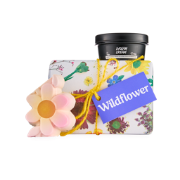Wildflower. A floral-wrapped box tied with yellow twine and a purple tag. A black pot of "Dream Cream" body lotion, and a pink and yellow flower-shaped soap sit around the box.