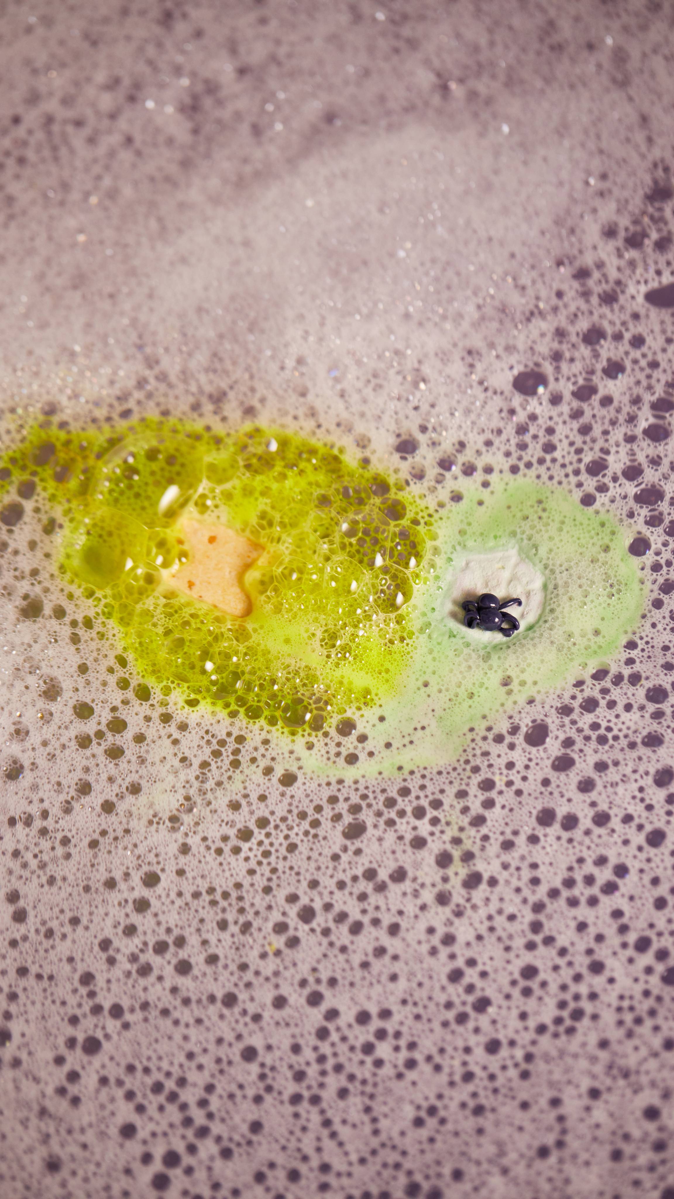 A close-up of the bubbly bathwater focusing on the luminous green surround the lightning bolt and spider web fun product.