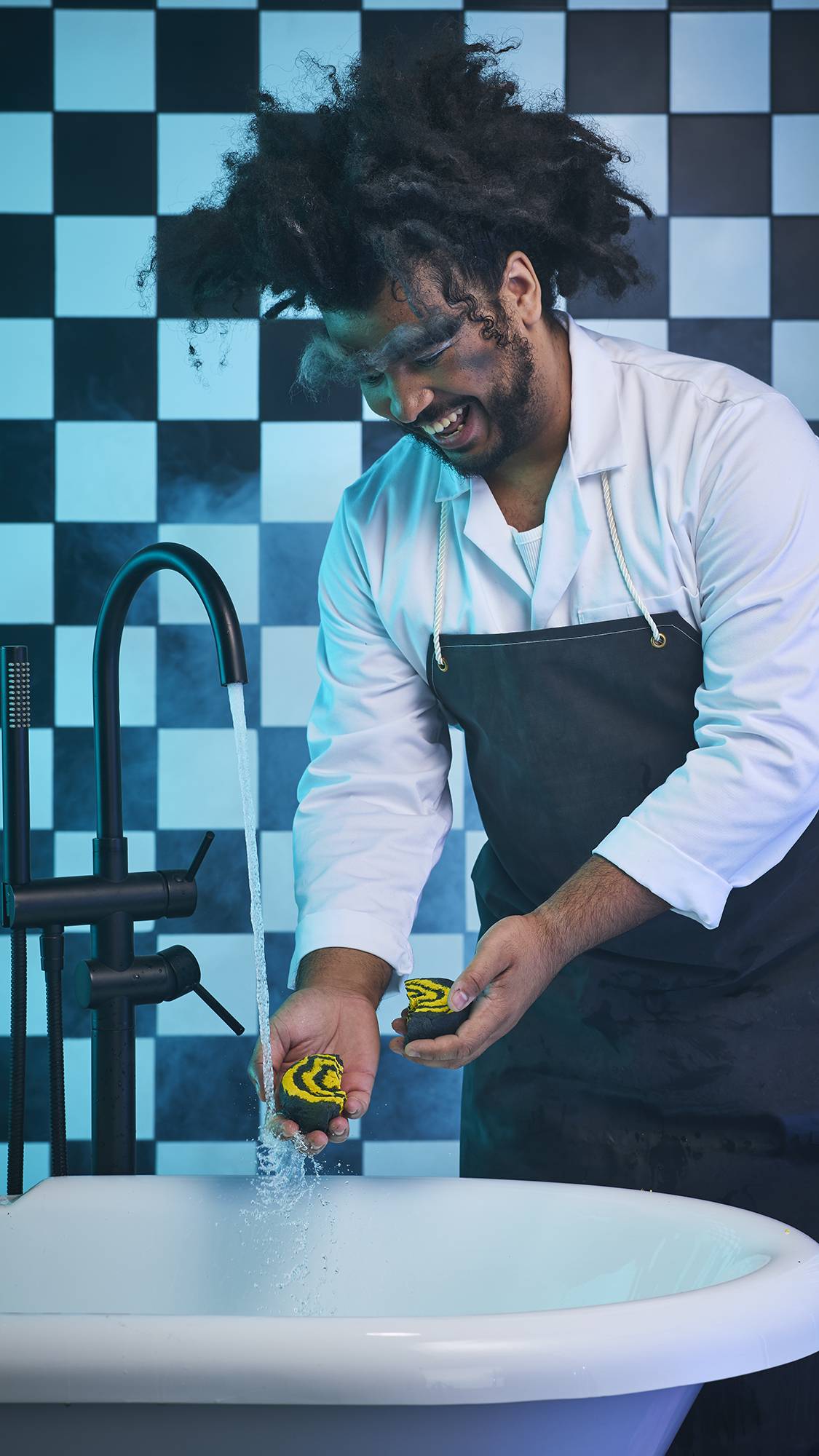 The image shows the model standing over the bath holding the Witchy Woo bubble bar under running tap water after having just broken it in half. There is a black and white checkered background with a blue hue. 