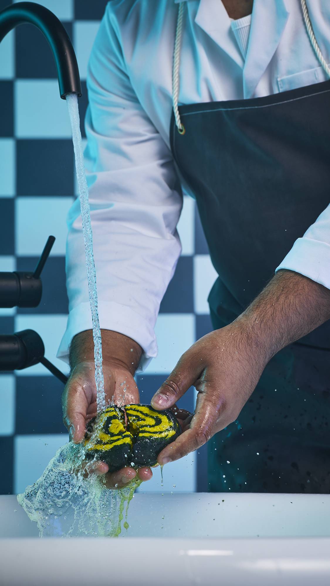 A close-up image of the mode's hand holding the Witchy Woo bubble bar under running tap water after having just broken it in half. There is a black and white checkered background with a blue hue. 