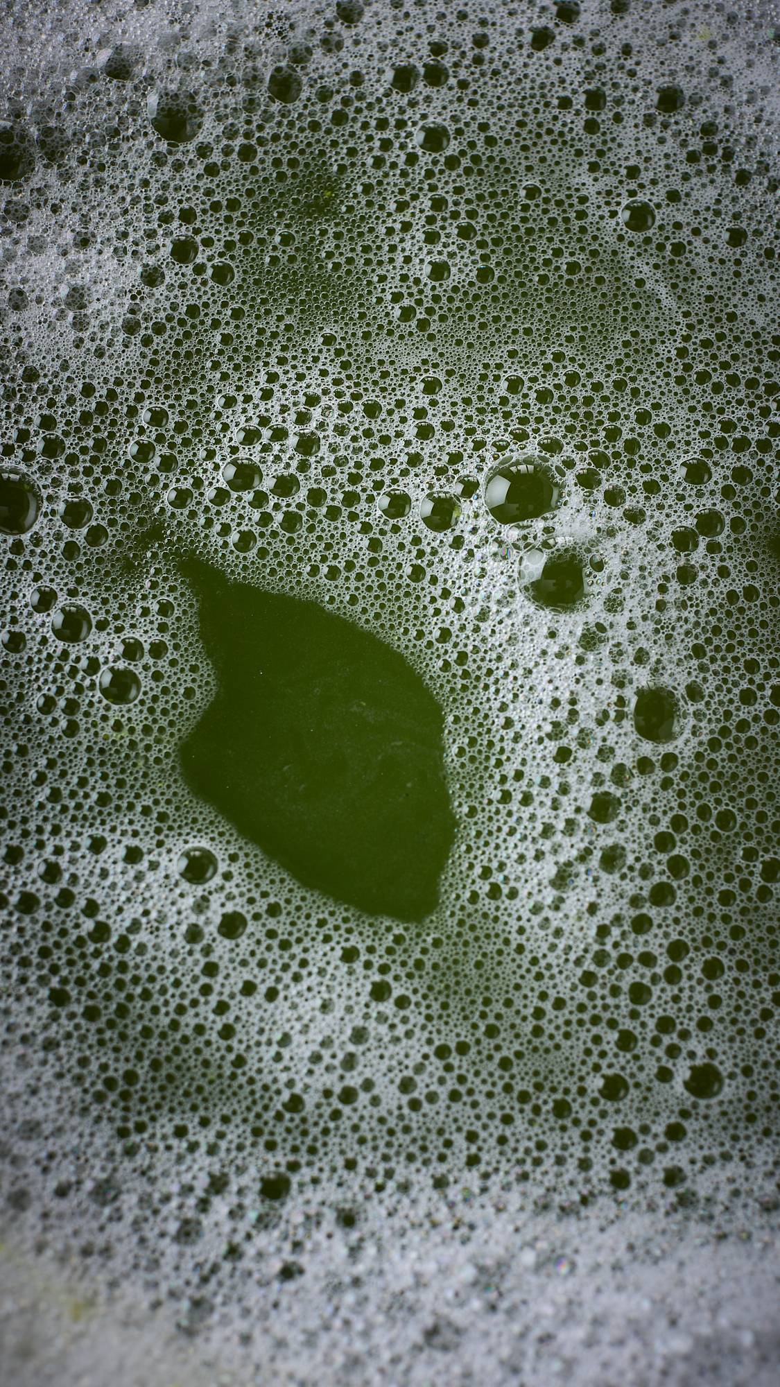 The image shows the aftermath of the Witchy Woo bubble bar showing deep, moss-green bath water and a layer of thick bubbles created from the product. 