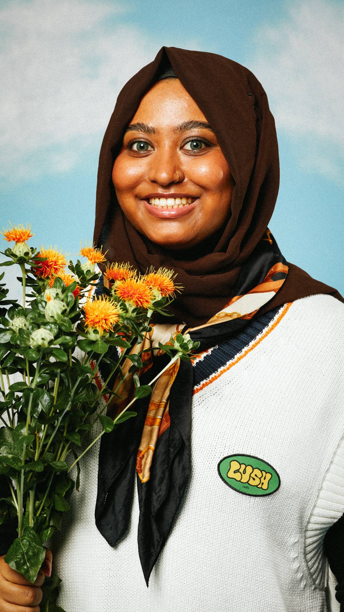 Model is wearing a hijab and white, knitted jumper with the Retro Bubble iron-on patch while they hold a bouquet of flowers. 
