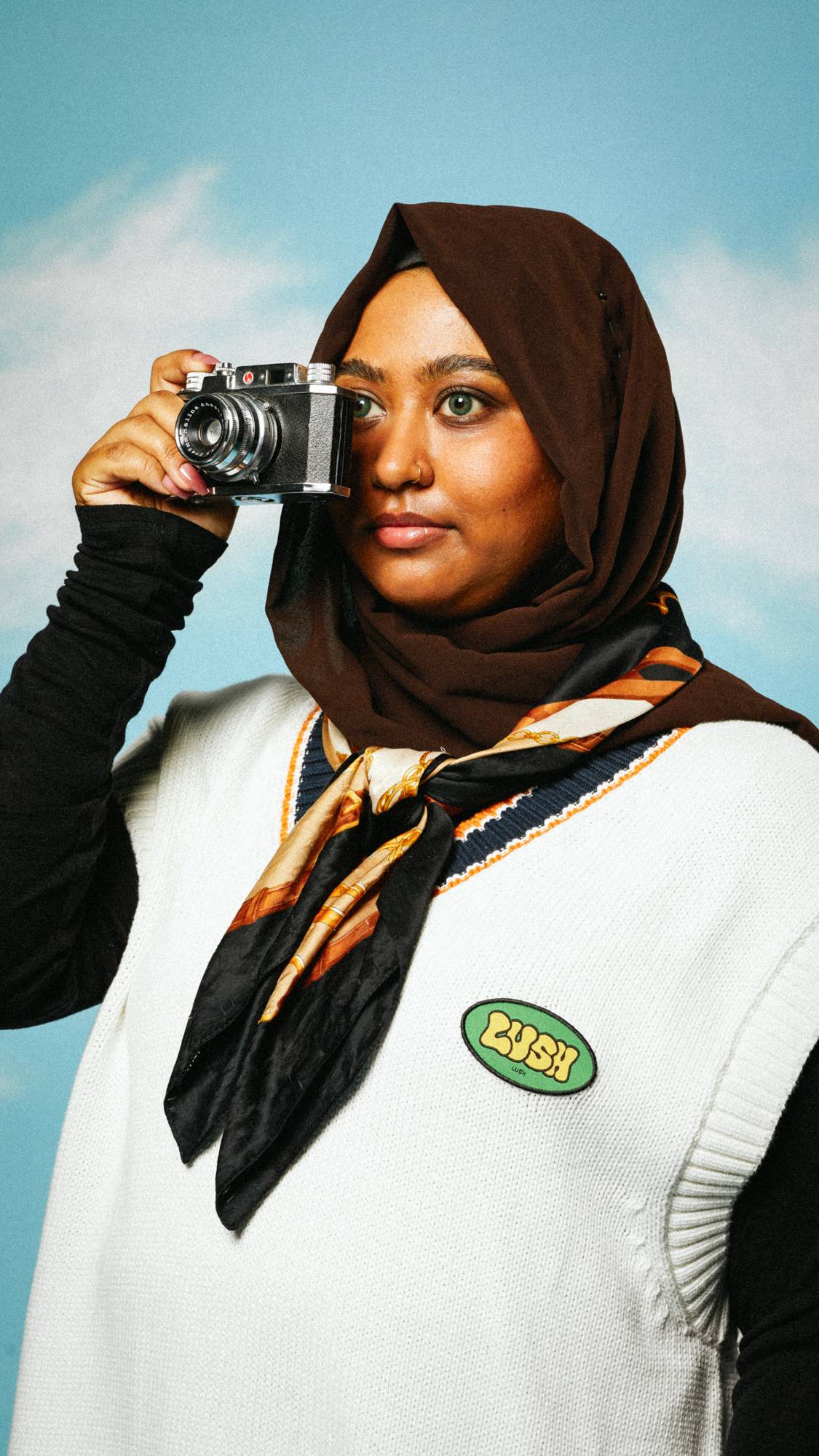 Model is wearing a hijab and white, knitted jumper with the Retro Bubble iron-on patch while they hold a camera for a photo. 