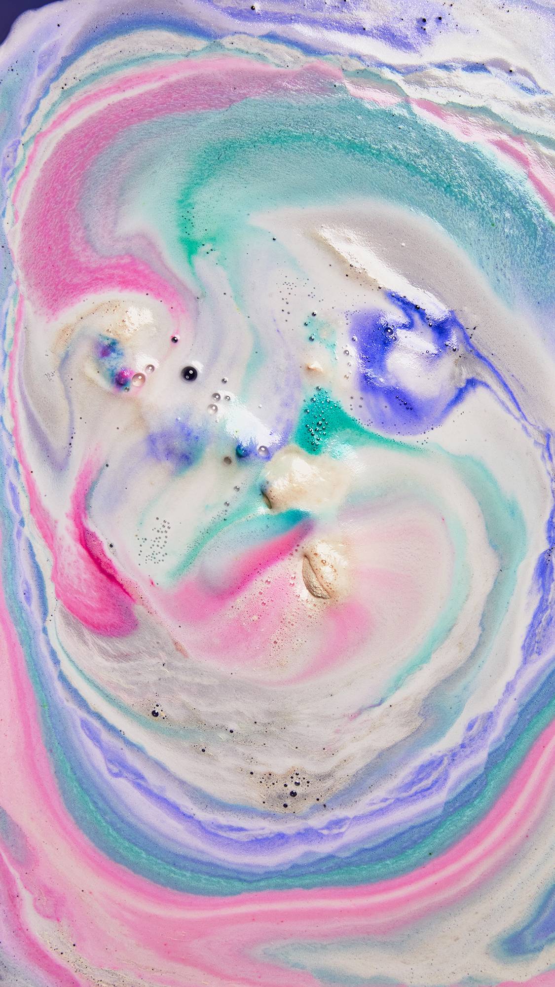 The image shows the aftermath of using the Xolo bath bomb showing vibrant, loose swirls of pink, teal, purple, blue and cream foam. 