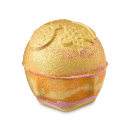 Yog Nog. A round, shimmering gold-coated bath bomb with an embossed Christmas-themed design on top and orange and pink marbled layers,