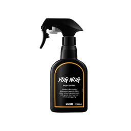 A recycled black plastic LUSH body spray bottle with a trigger nozzle stands upright with an orange-rimmed black label that reads "Yog Nog Body Spray". The product description is printed in white text.