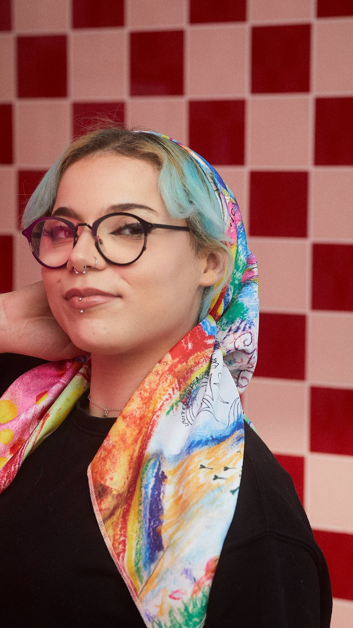 The model is stood in front of a red, tiled background. They have fashioned the You Are Amazing knot wrap into a trendy head scarf. 
