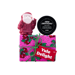 A Lush Yule Delight gift set wrapped in patterned pink paper with green twine, topped with a red Father Christmas soap and a black tub of Yuzu Cheesecake body butter