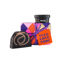 Yule Love This! An off-square gift box wrapped in diamond-patterned colourful paper, tied with a purple ribbon and orange gift tag. Two Christmas-themed products sit around the box.