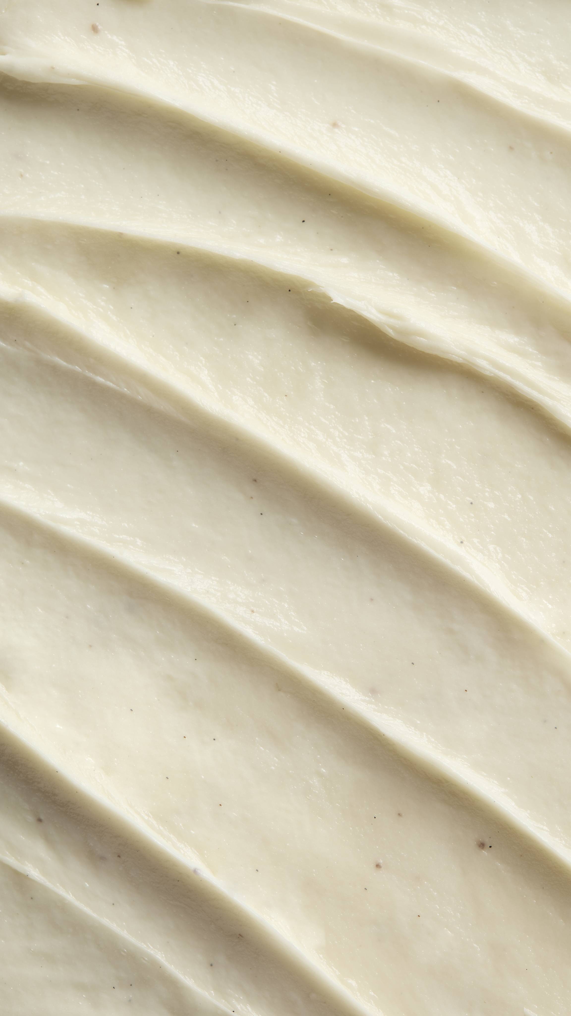 A close-up shows the thick, pale yellow texture of "Yummy Custard" body wash spread in diagonal ridges with tiny black vanilla specks.