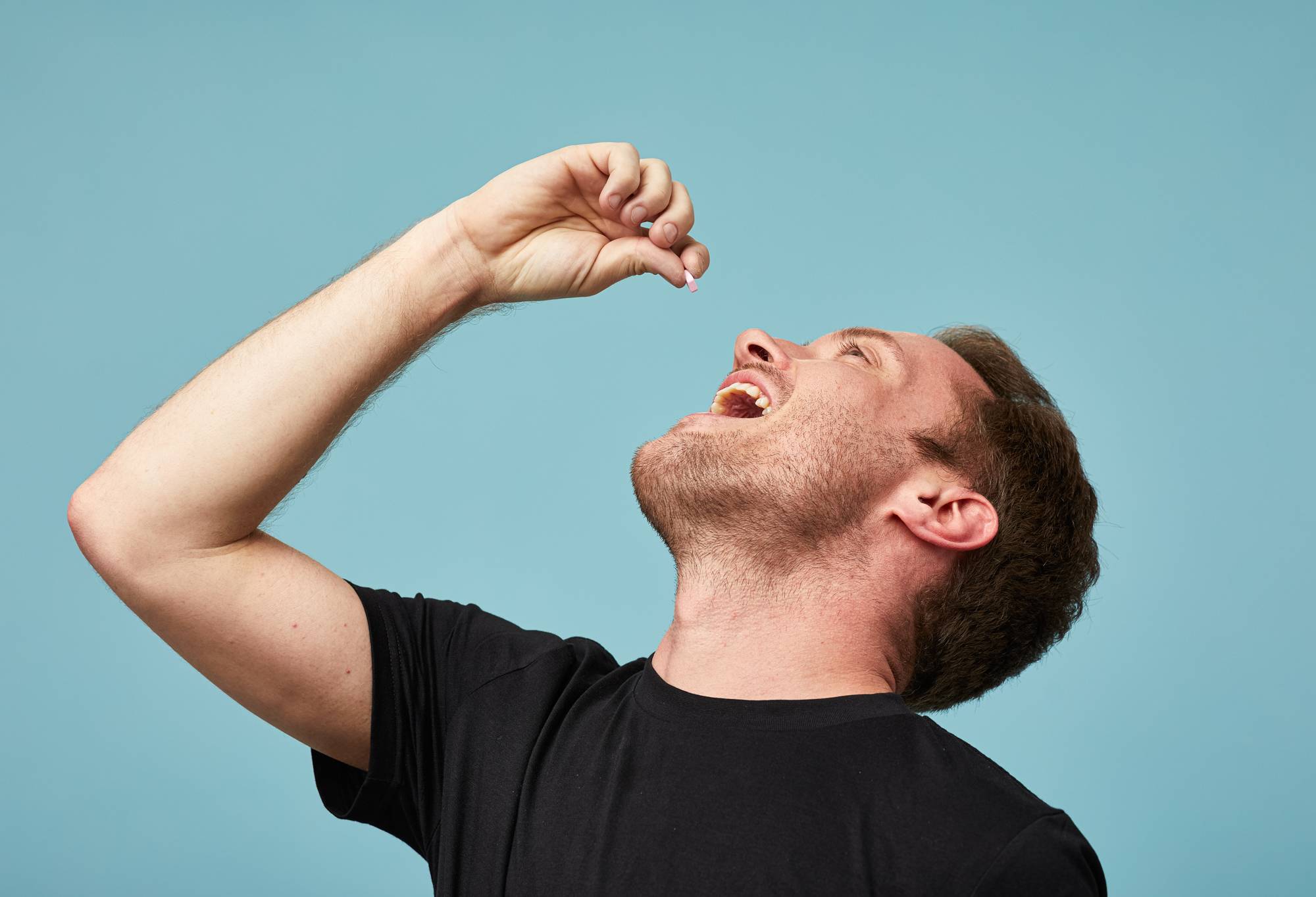 A person prepares to put a small pink mouthwash tab into their open mouth with their hand.