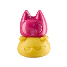 A glossy pink, cat-like shower gummy head sits stacked directly on a matte yellow body scrub base featuring engraved sunglasses. White background.